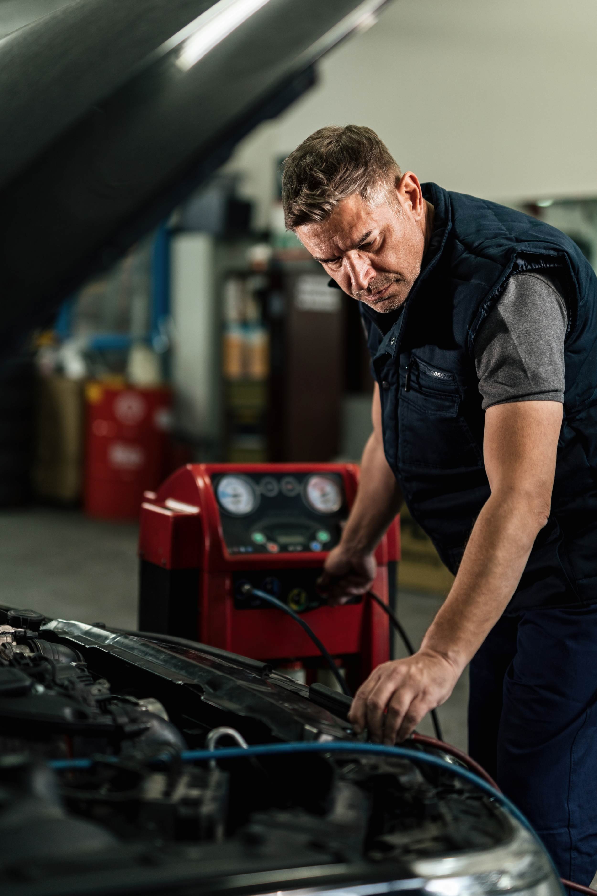 A mechanic working on a car engine in a garage, with a red diagnostic scanner nearby.