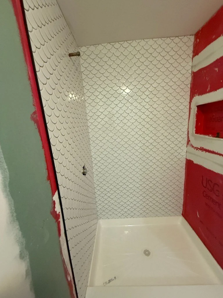 Shower stall with scale-patterned ceramic wall tiles and unfinished walls around.