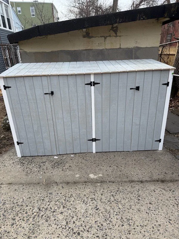 Gray outdoor storage shed with black hinges on concrete surface.