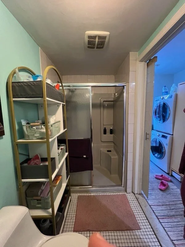 Bathroom with shower, metal shelves, sink, and a doorway leading to a laundry room with washer and dryer.