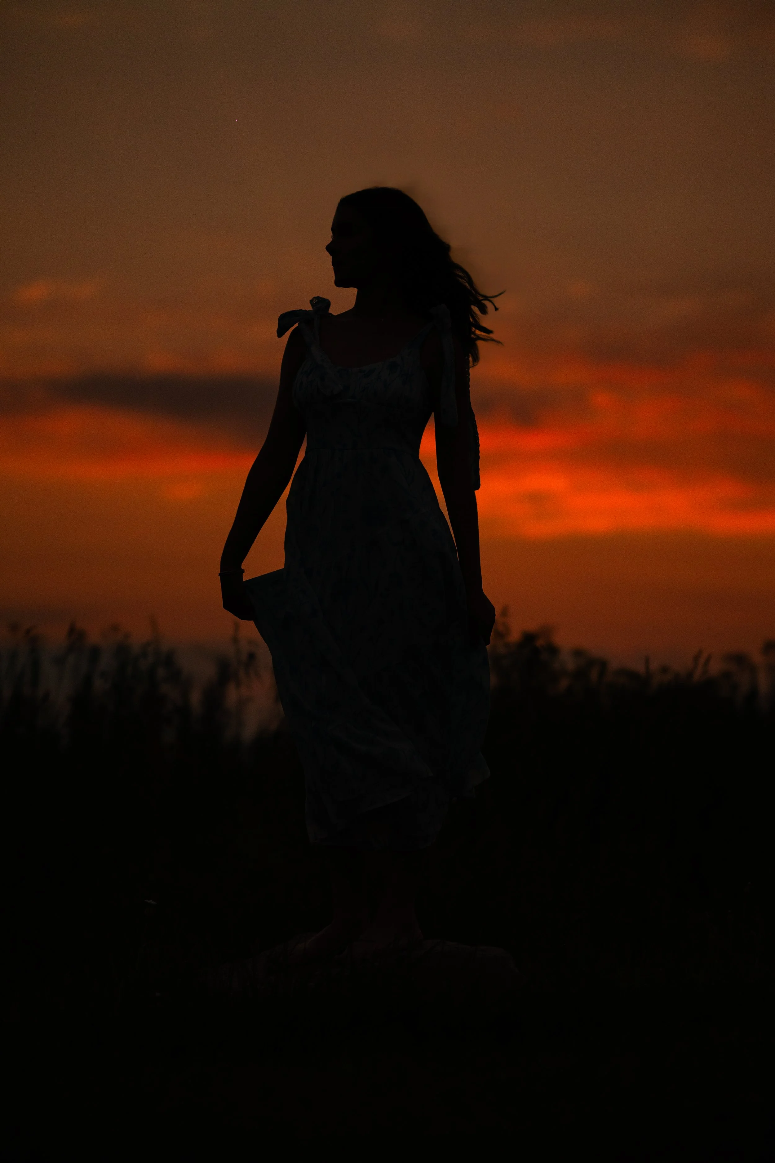 Senior girl in silhouette in a dress in a flower field at golden hour sunset.