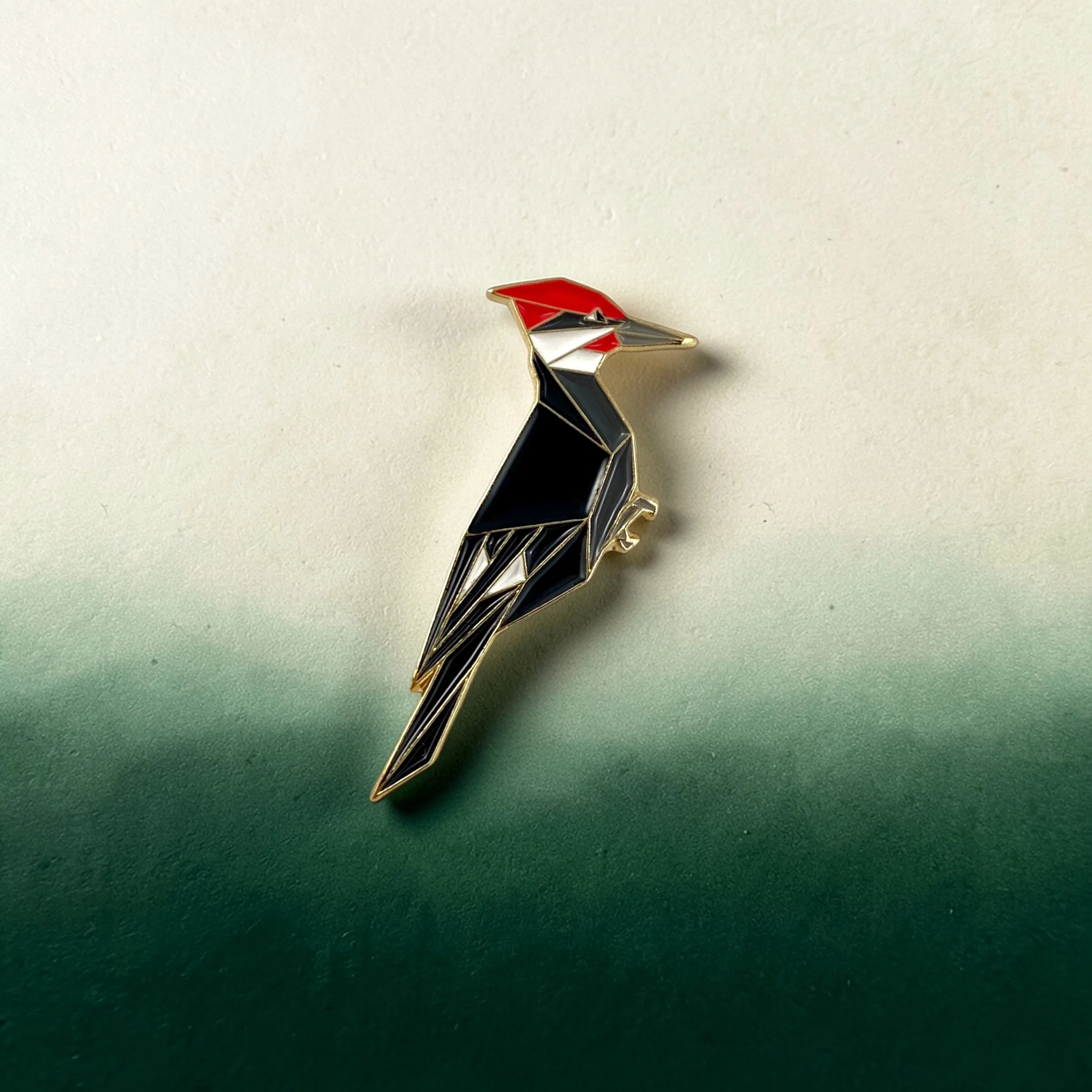 Origami pileated woodpecker enamel pin – a unique bird themed gift for bird lovers and bird watchers. Soft enamel pin with secure double pin backing and original FoldIT Creations design.