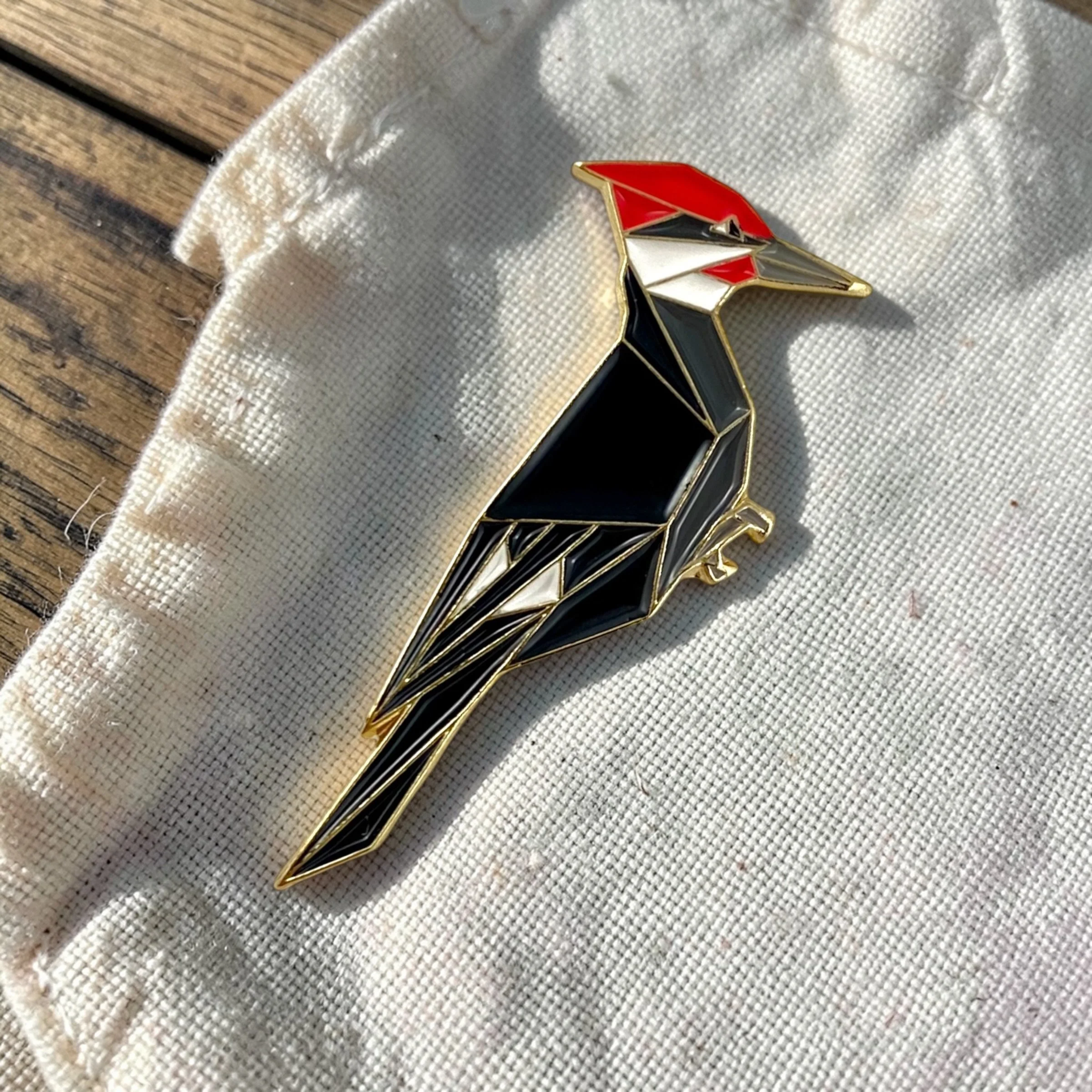 Origami pileated woodpecker enamel pin – a unique bird themed gift for bird lovers and bird watchers. Soft enamel pin with secure double pin backing and original FoldIT Creations design.