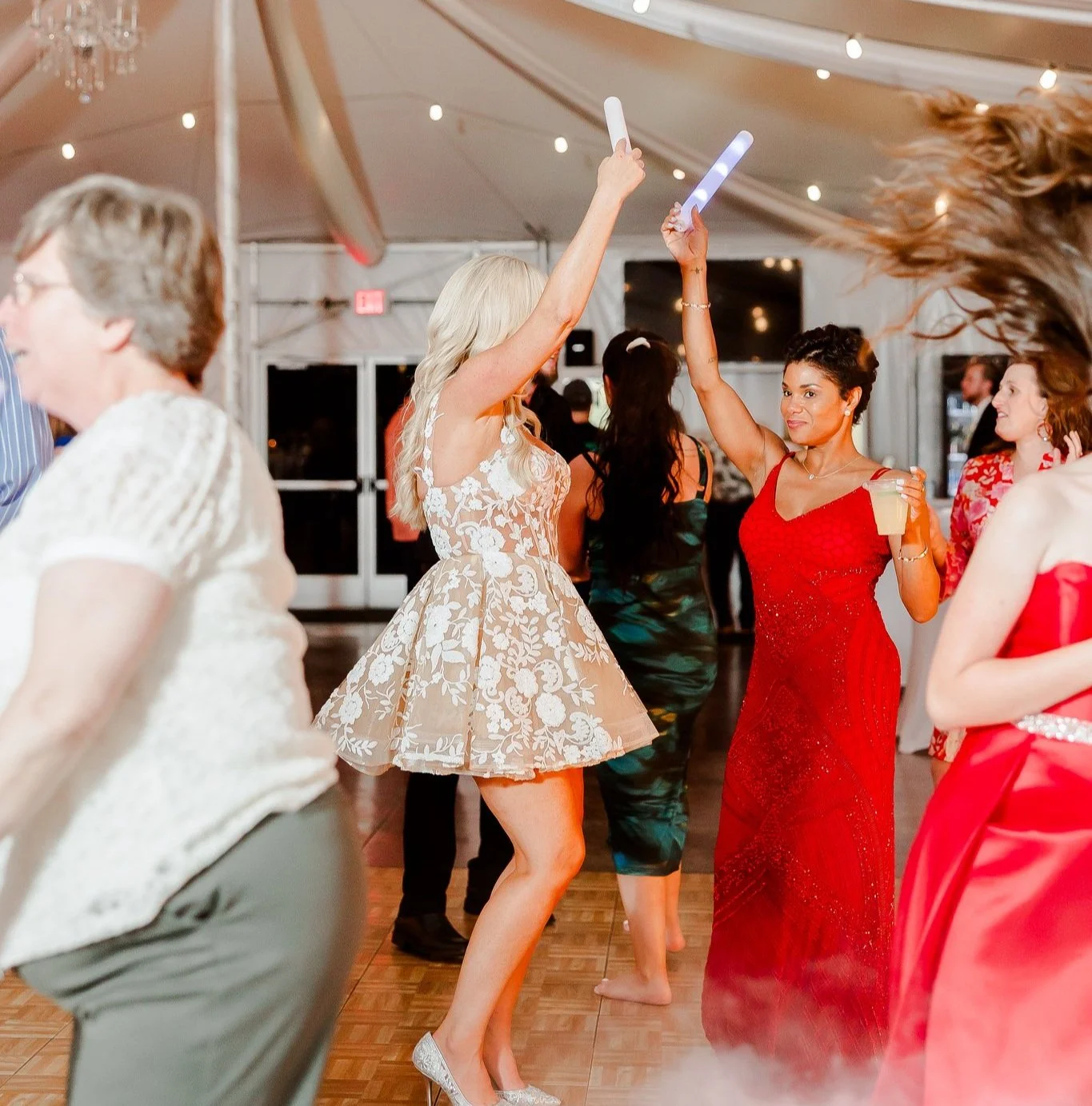 People dancing at a party, woman in beige floral dress and woman in red dress with light sticks in the event tent venue in New Town St. Charles, MO..