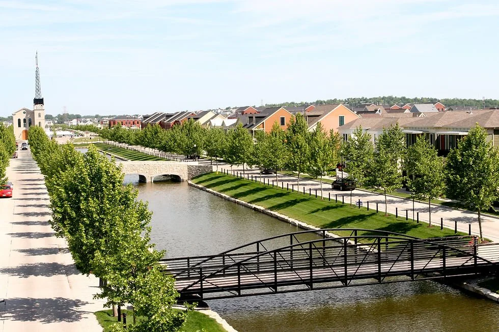 An arial view of New Town St. Charles, MO overlooking the canal, bridges, trees, houses, and a church with a tall steeple.