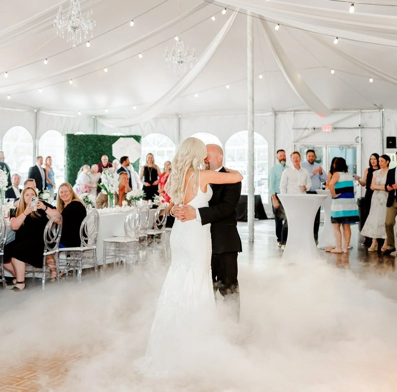 A bride and groom sharing their first dance at a wedding reception inside The Marquee at New Town event tent, with guests watching and taking photos while a cloud shimmers up from the floor.
