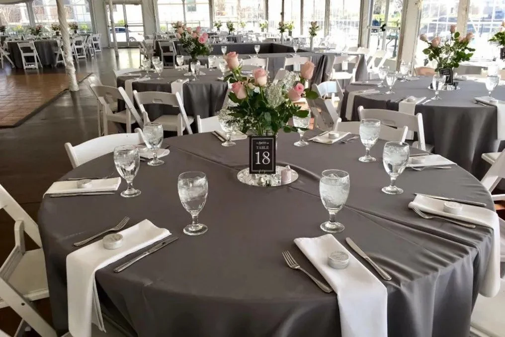 Perfectly decorated wedding reception at The Marquee at New Town with round tables dressed with linens, water goblets, a centerpiece of light pink roses and black table number plaques.