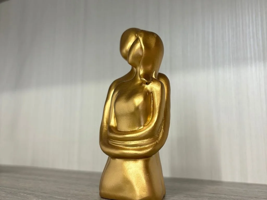 Escultura dorada de pareja abrazándose en una estantería de madera.