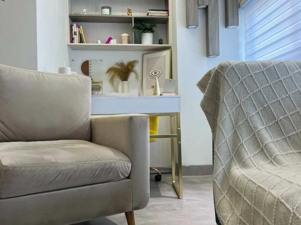 Sala moderna con sillón gris, mesa blanca con decoraciones y estantería con libros y adornos.