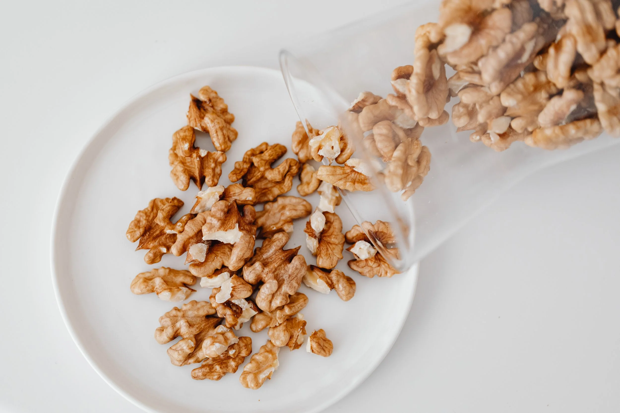 A white plate holding several walnuts, with some walnuts spilling onto a nearby surface.