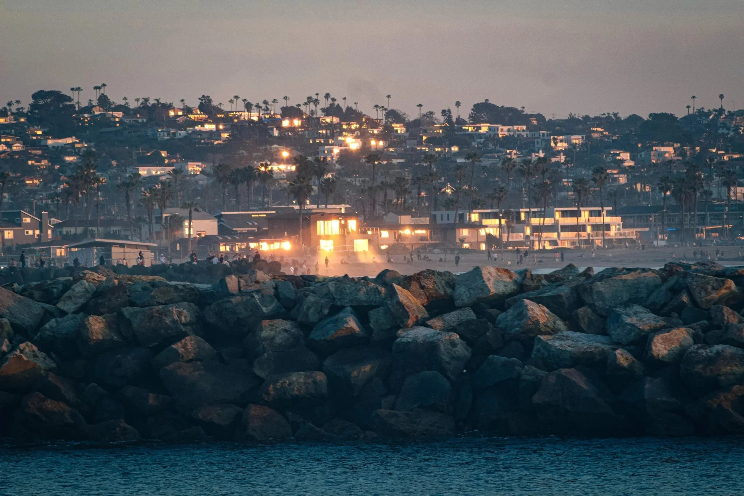 Beach town lights behind a rock jetty at dusk, San Diego, California - fine art print by Zyan Sachs