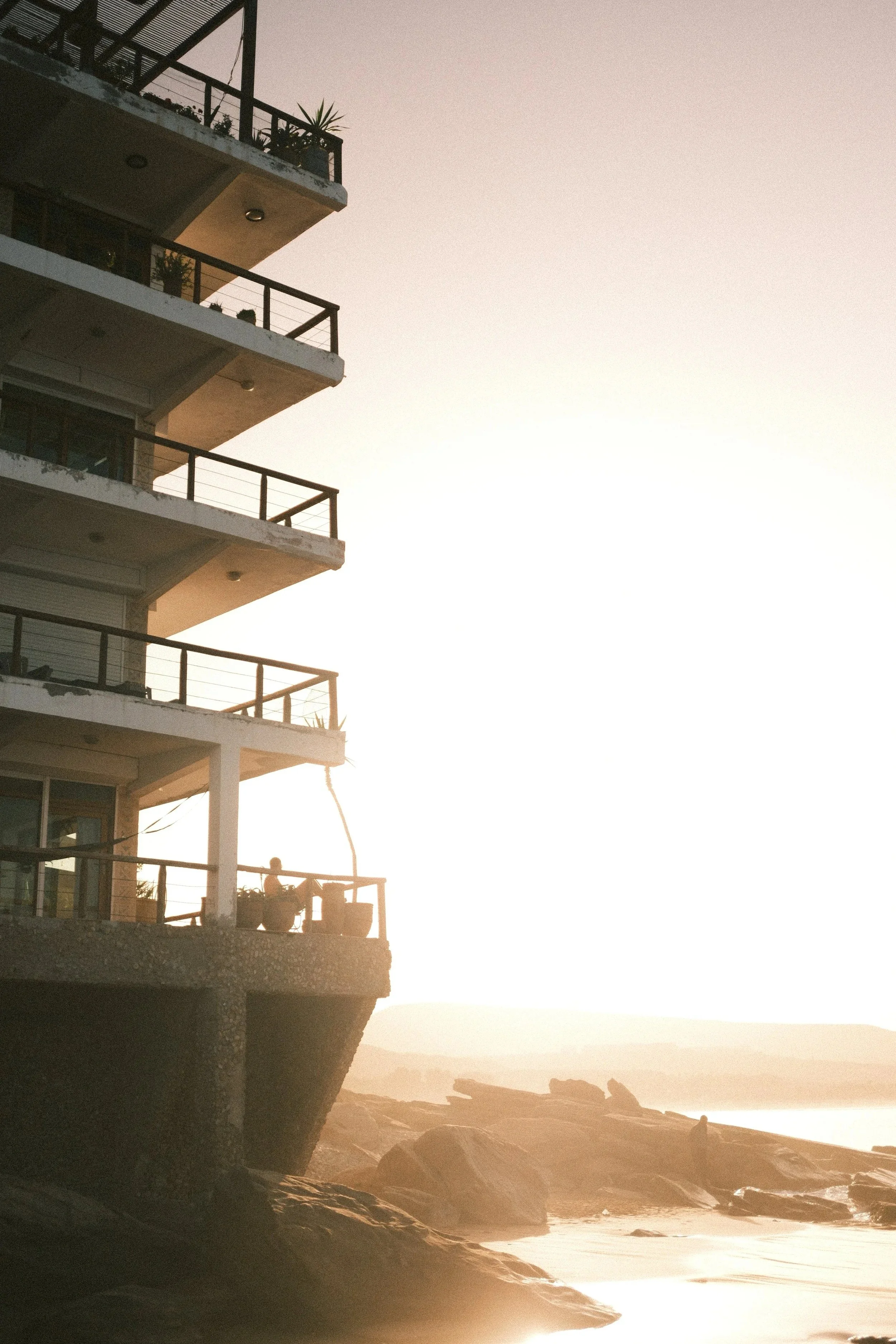 Sun flaring behind a balconied apartment building by the sea, Taghazout, Morocco - fine art print by Zyan Sachs