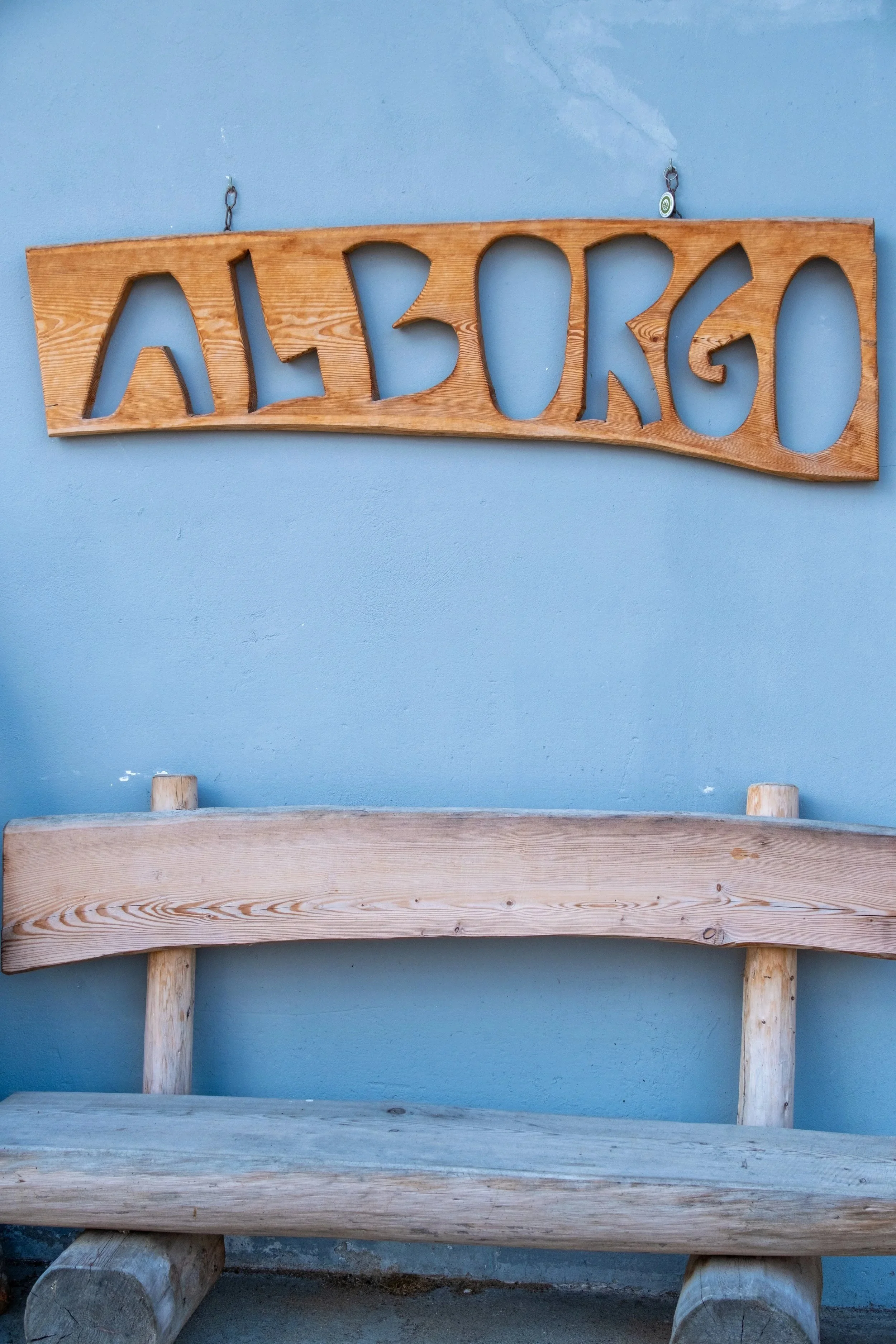Carved wooden Al Borgo sign above a bench on a blue wall at Al Borgo da Agata, Dolomites, Italy, by Zyan Sachs