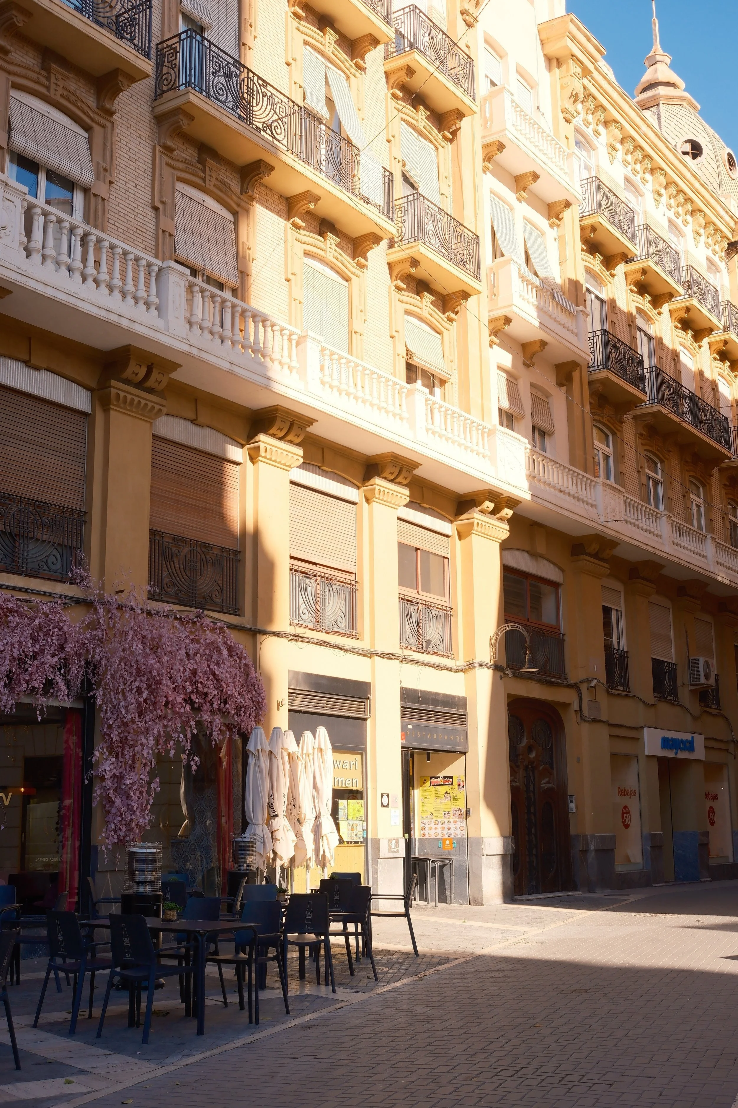 Golden morning light on ornate balconies and café tables along a street in Murcia, Spain - fine art print by Zyan Sachs