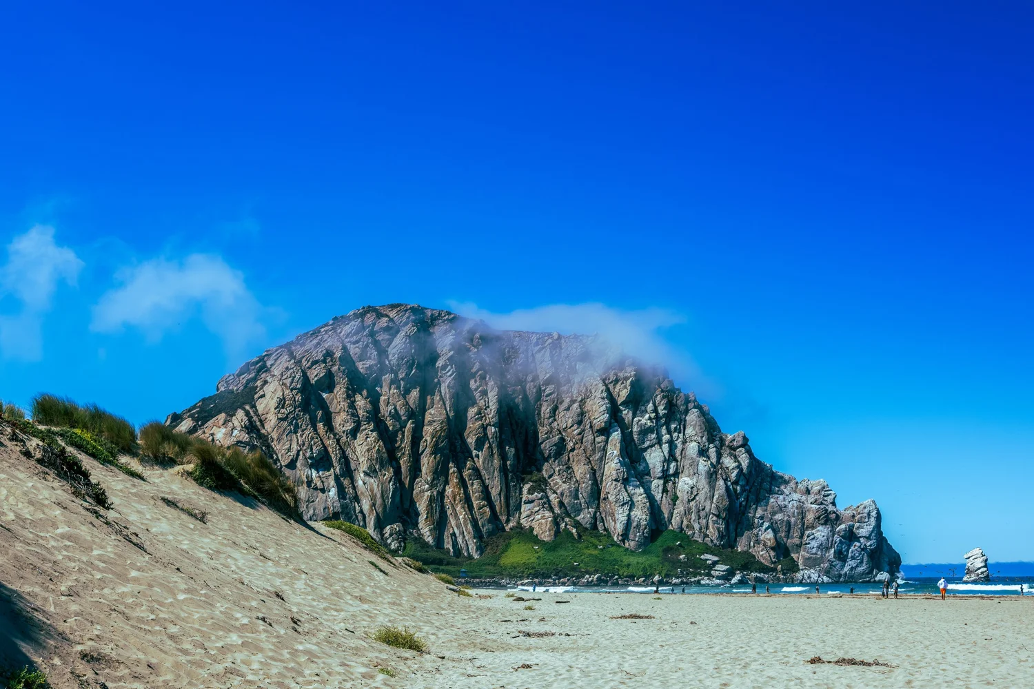 Morro Rock rising beyond the dunes under a blue sky, Morro Bay, California - fine art print by Zyan Sachs