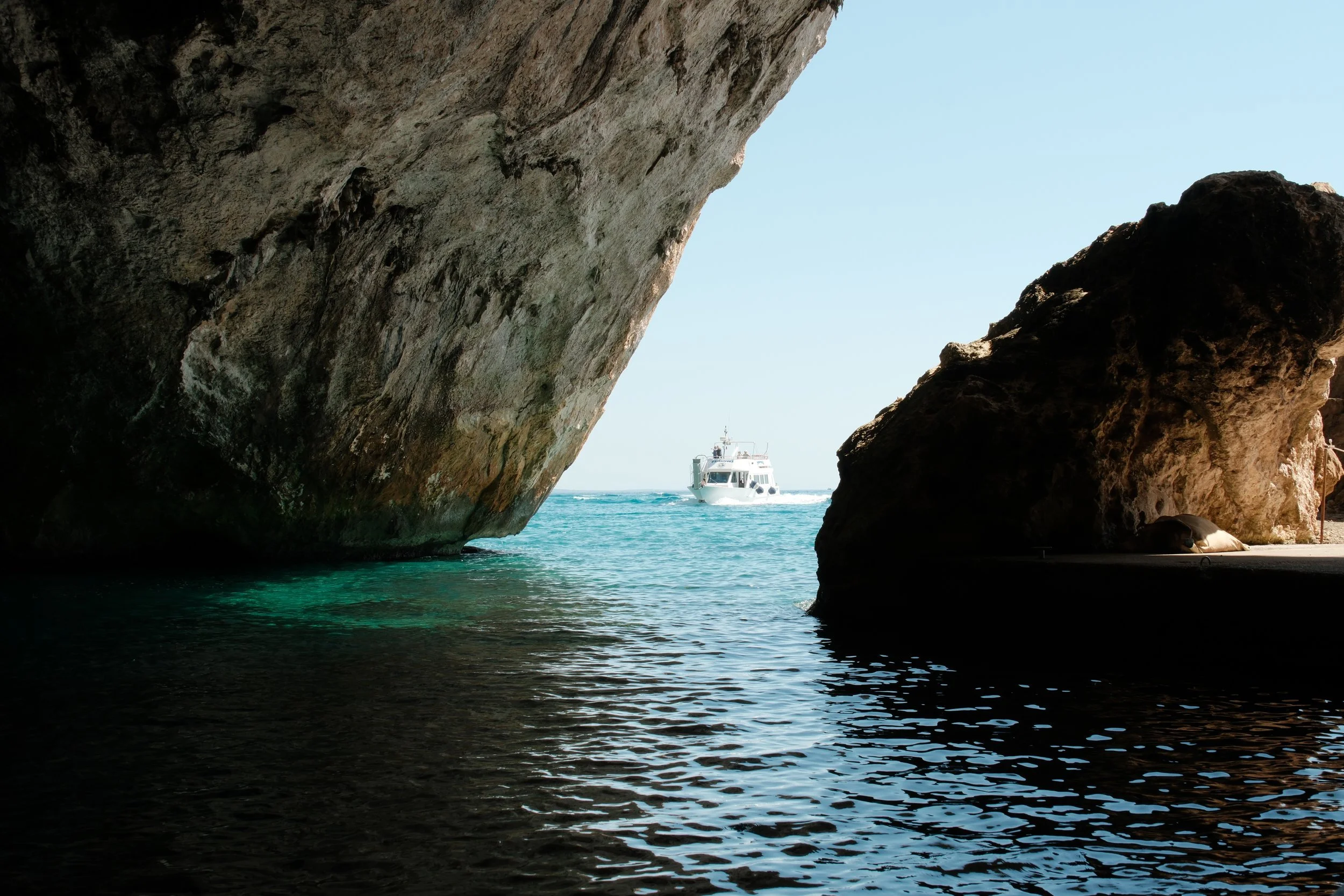 Boat framed by the mouth of a sea cave above turquoise water, Gulf of Orosei, Sardinia, Italy, by Zyan Sachs