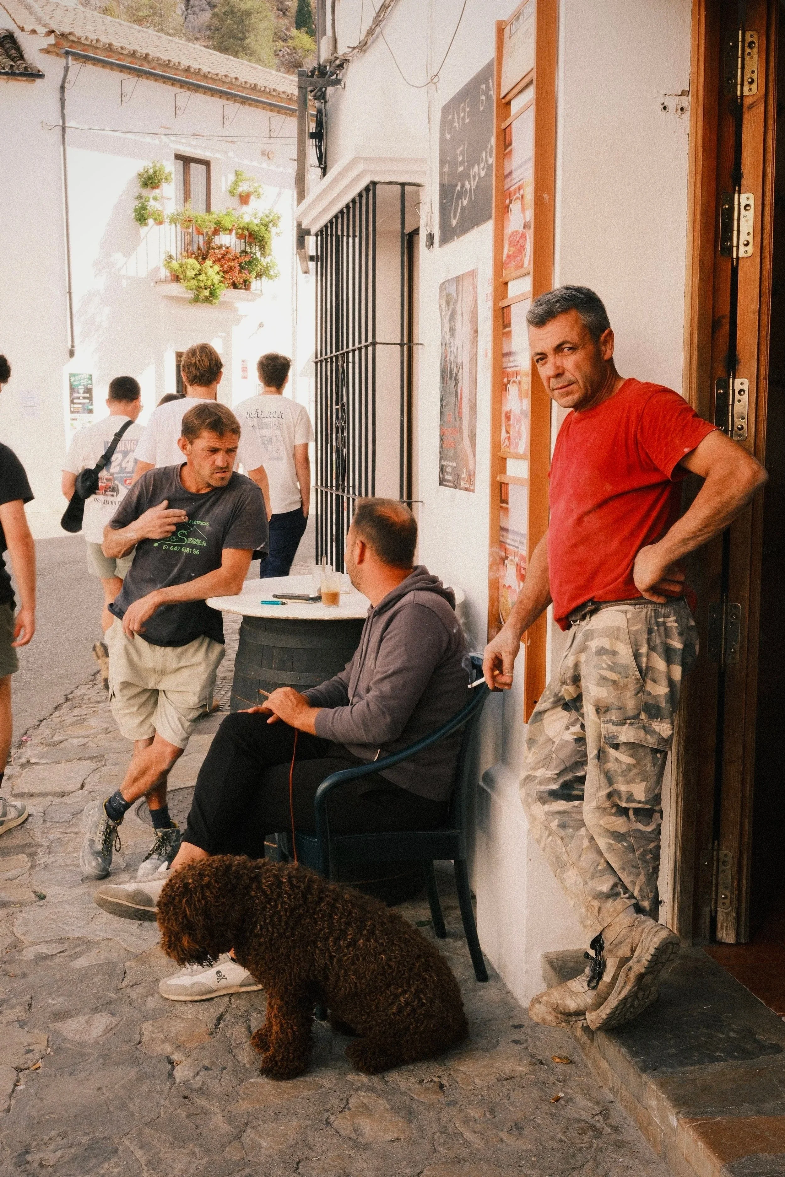 Men chatting outside a café on a whitewashed street in Grazalema with a brown water dog, Andalusia, Spain - fine art print by Zyan Sachs