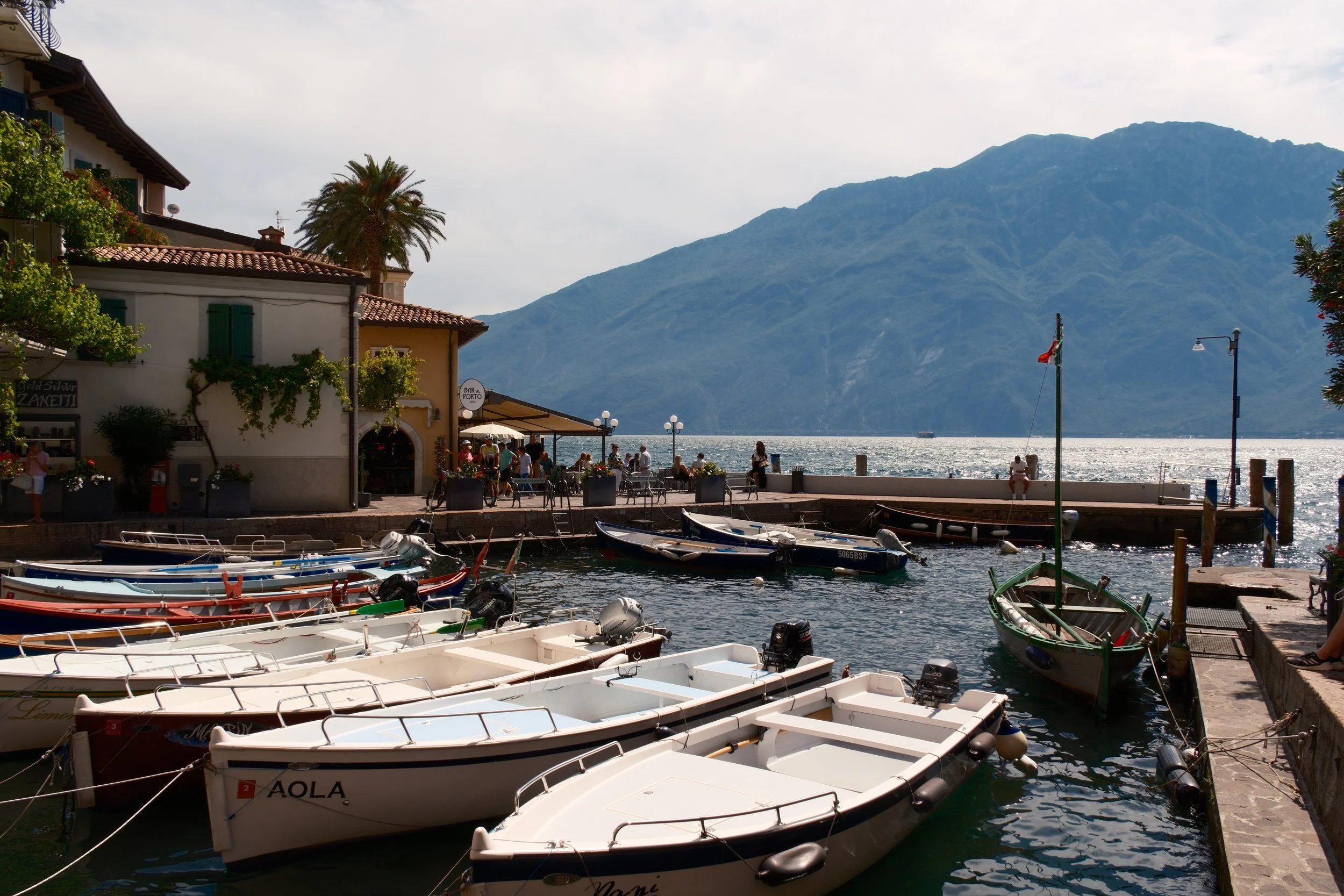 Small harbor of Limone sul Garda with white boats, a café and Monte Baldo across the lake, Lake Garda, Italy, by Zyan Sachs