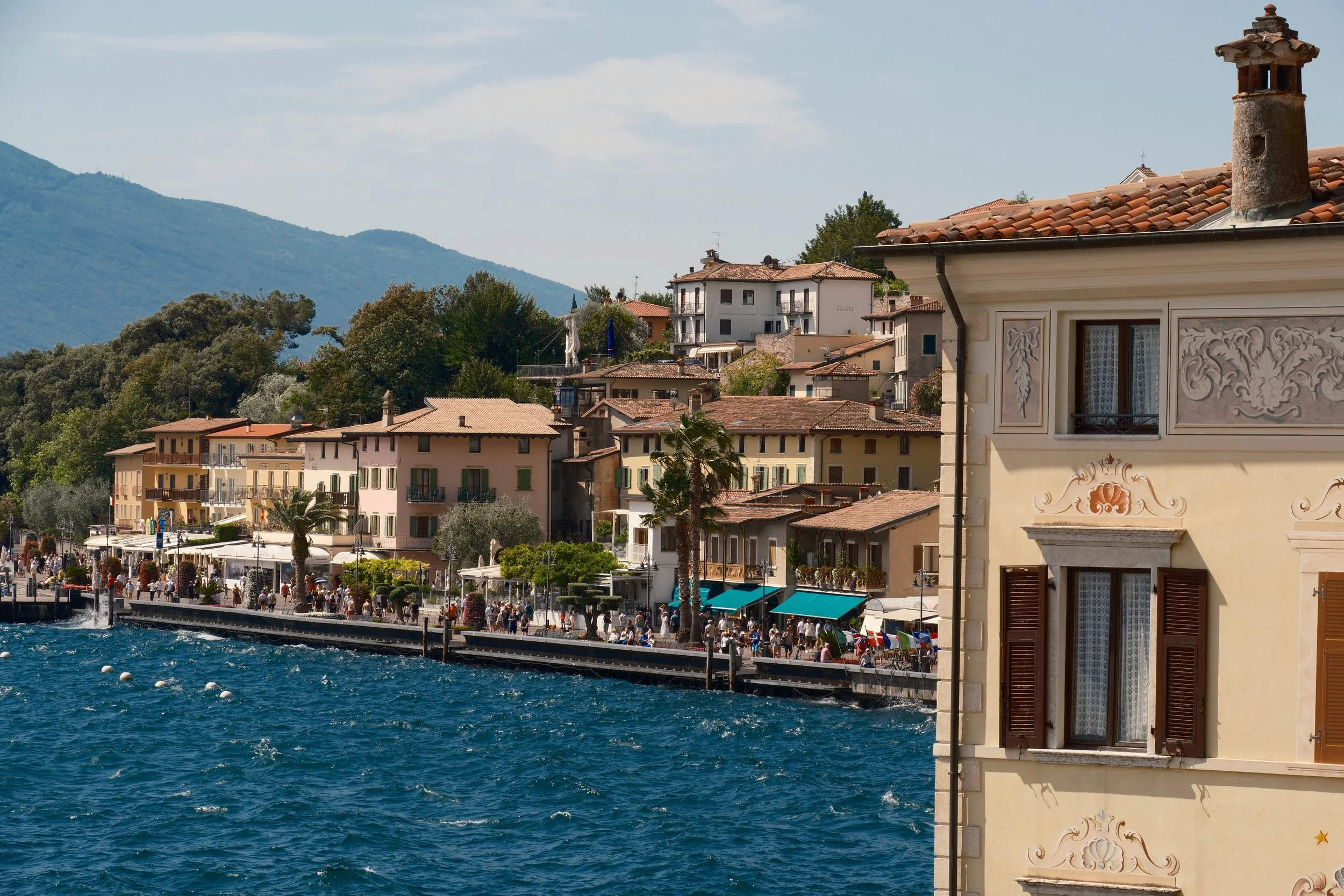 Busy lakefront promenade of Limone sul Garda beside a frescoed building and windswept blue water, Lake Garda, Italy, by Zyan Sachs