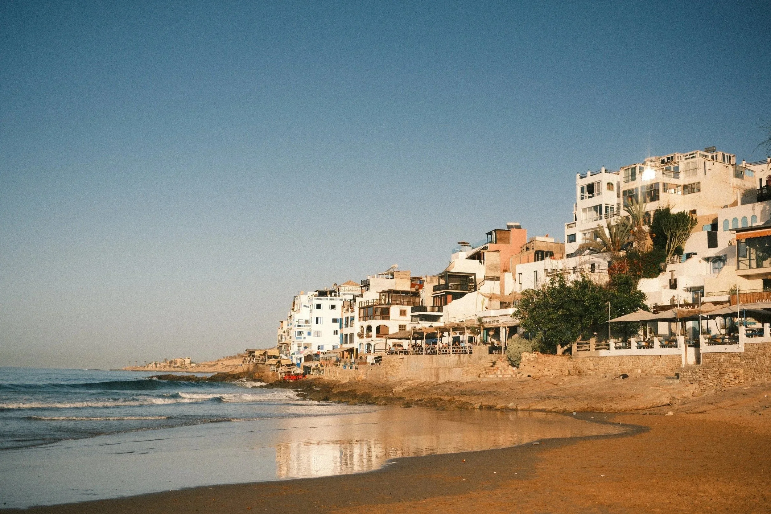 White and terracotta houses along the curve of the bay, Taghazout, Morocco - fine art print by Zyan Sachs