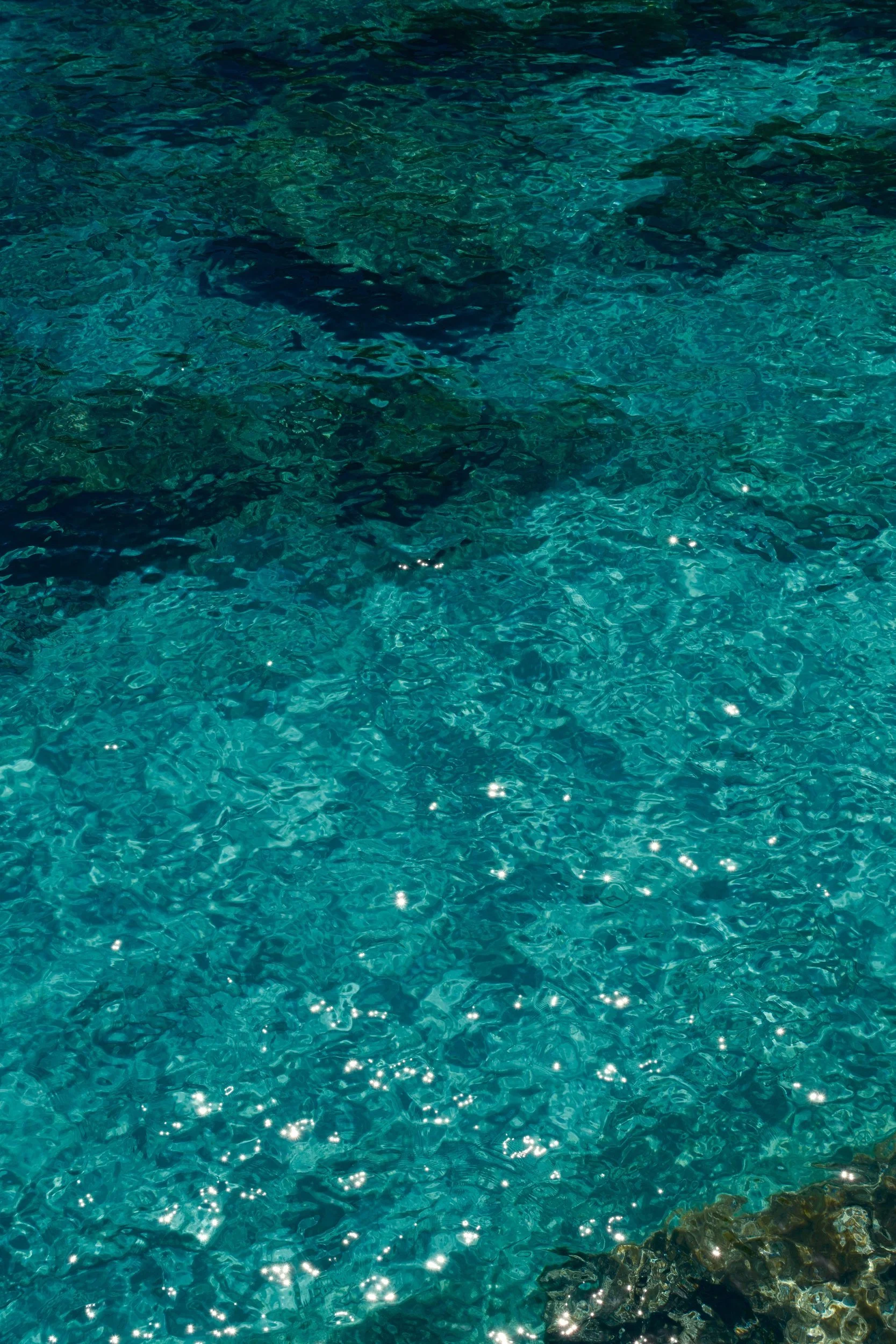 Sunlight sparkling on clear turquoise Mediterranean water over rocks, Sardinia, Italy, by Zyan Sachs
