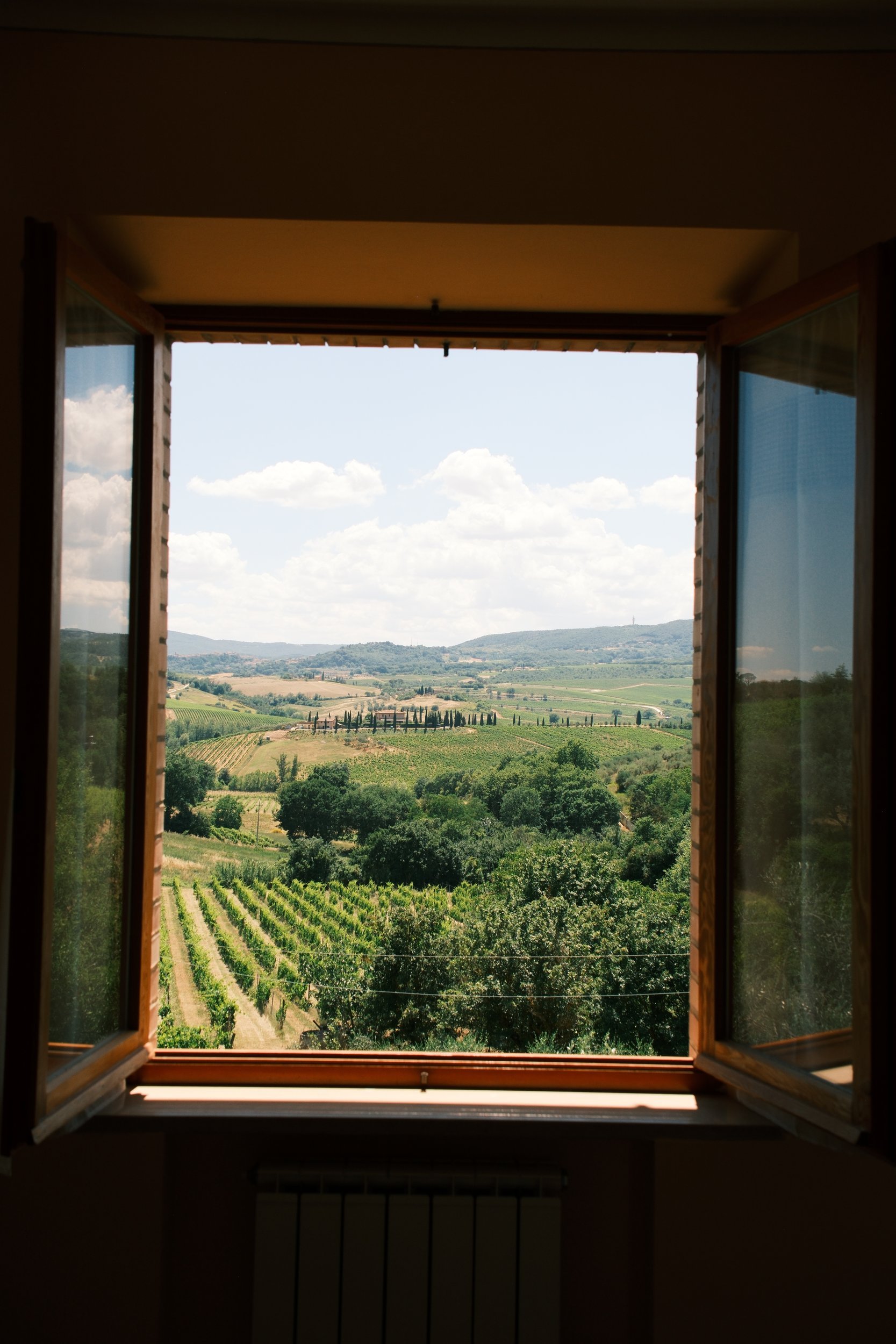 View through an open farmhouse window over vineyards and cypress-lined hills, Tuscany, Italy, by Zyan Sachs