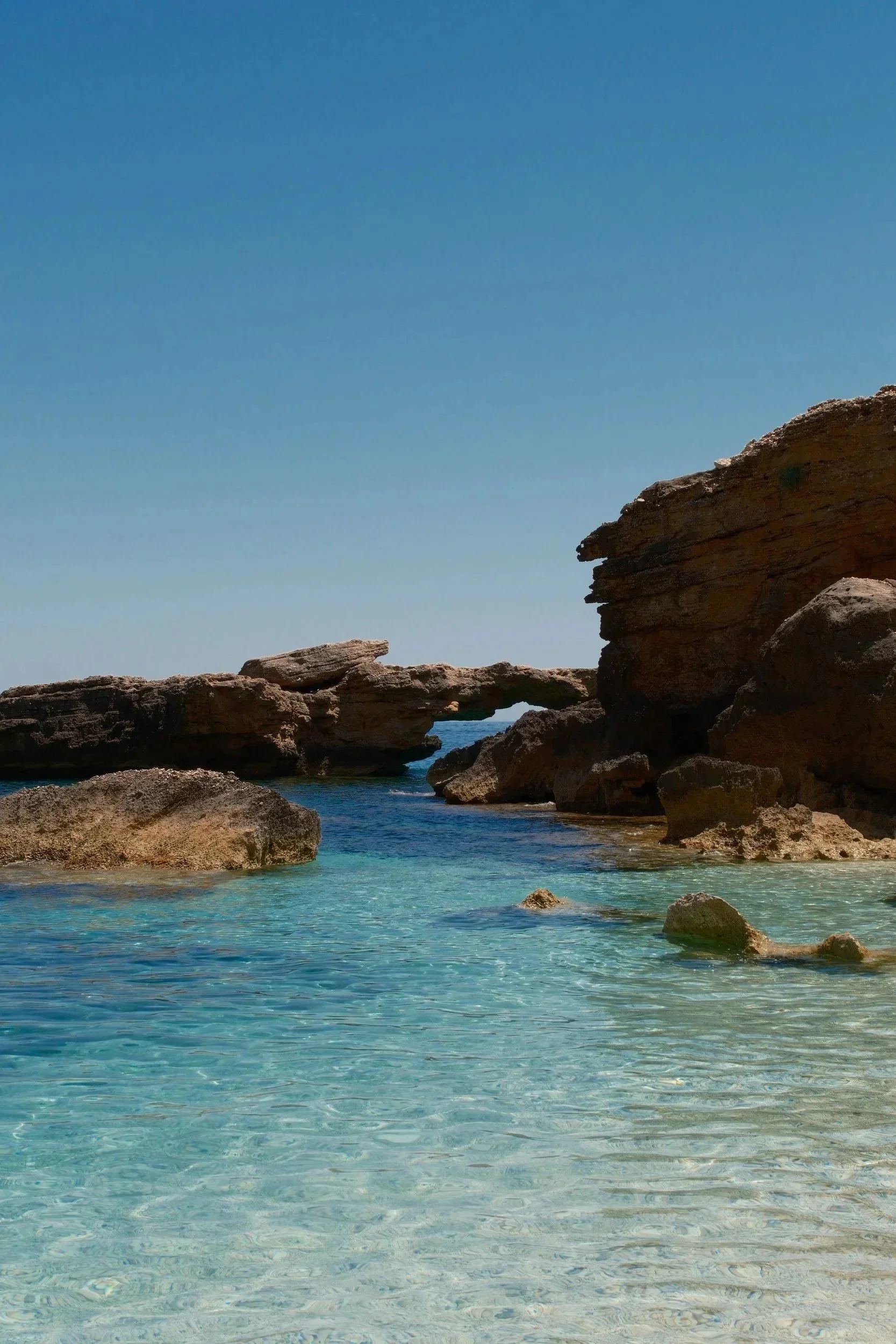 Crystal-clear turquoise shallows below a natural rock arch, Sardinia, Italy, by Zyan Sachs