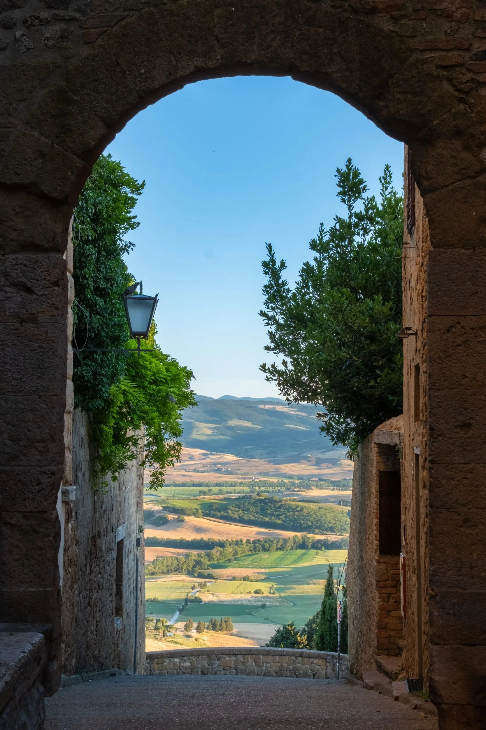 Medieval stone archway framing a view of the Tuscan valley and farmland below, Italy, by Zyan Sachs