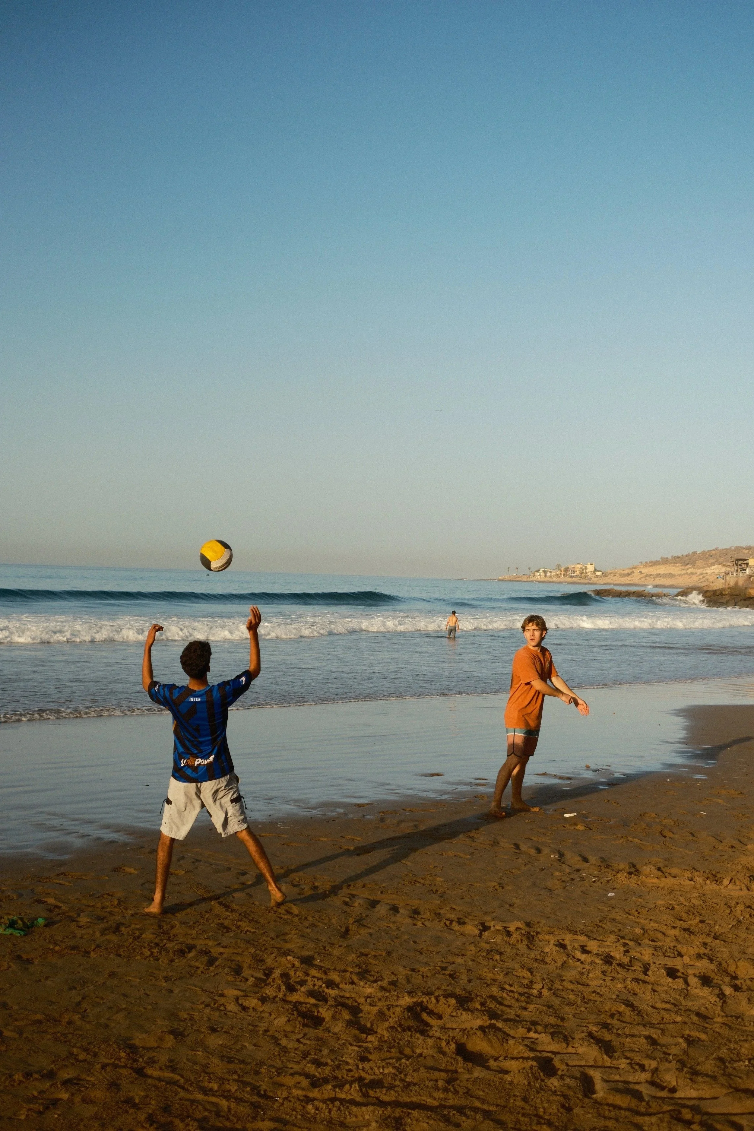 Kids playing on the beach with the town behind, Taghazout, Morocco - fine art print by Zyan Sachs