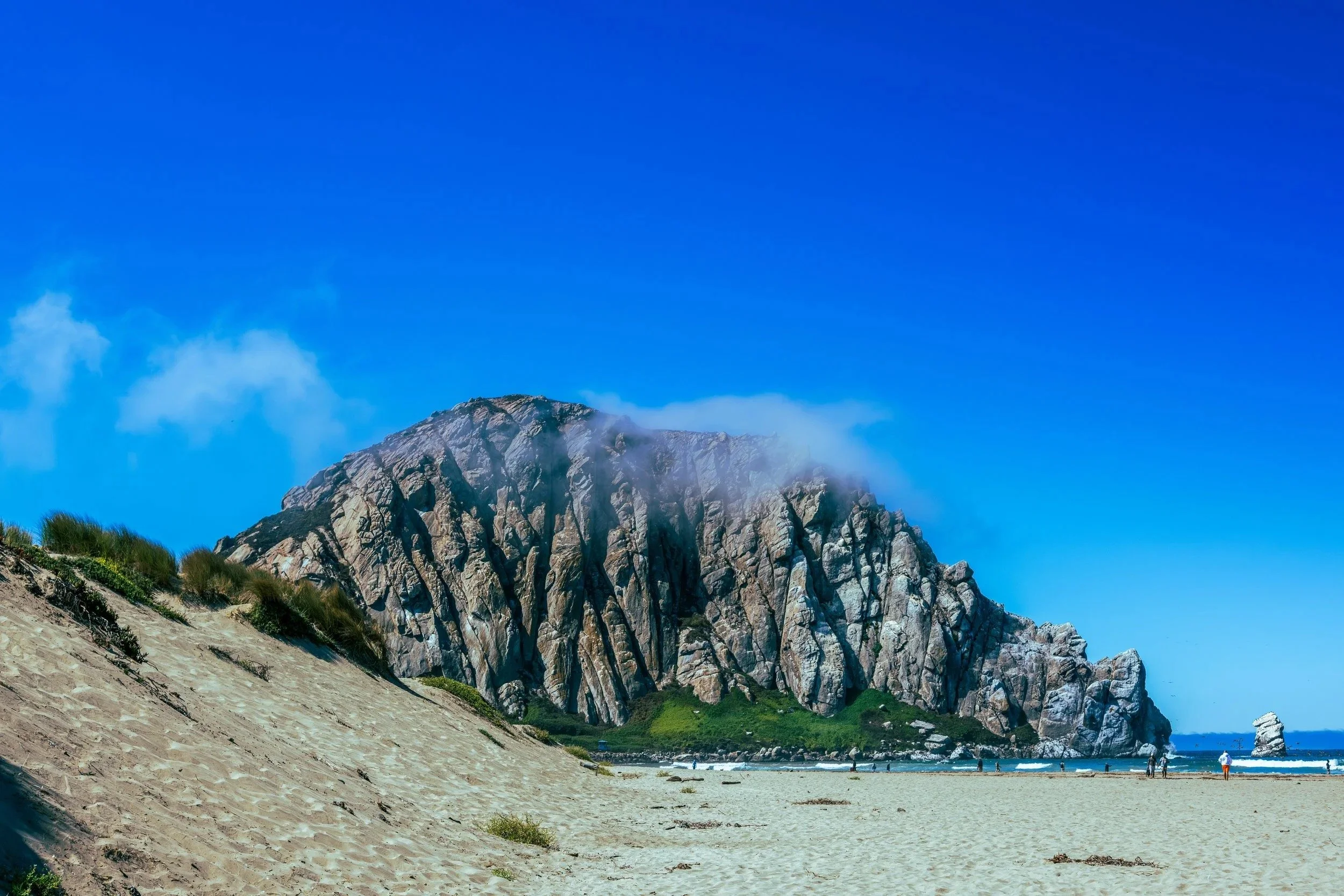 Morro Rock rising beyond the dunes under a blue sky, Morro Bay, California - travel photography and fine art prints by Zyan Sachs