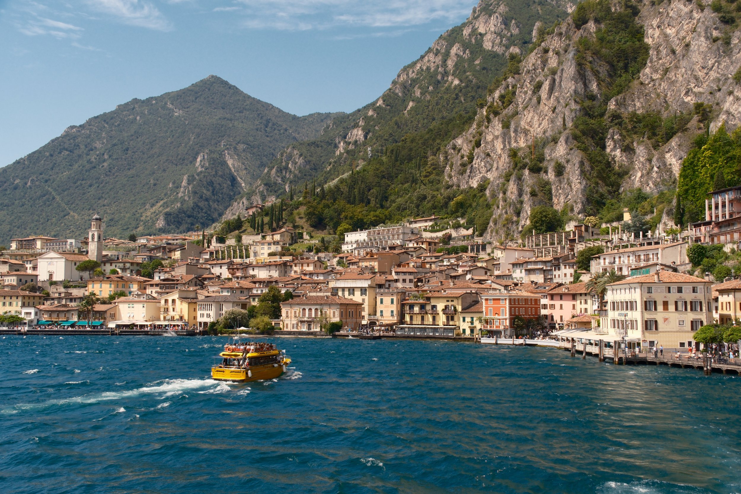 Yellow tour boat crossing toward Limone sul Garda beneath limestone cliffs and mountains, Lake Garda, Italy, by Zyan Sachs