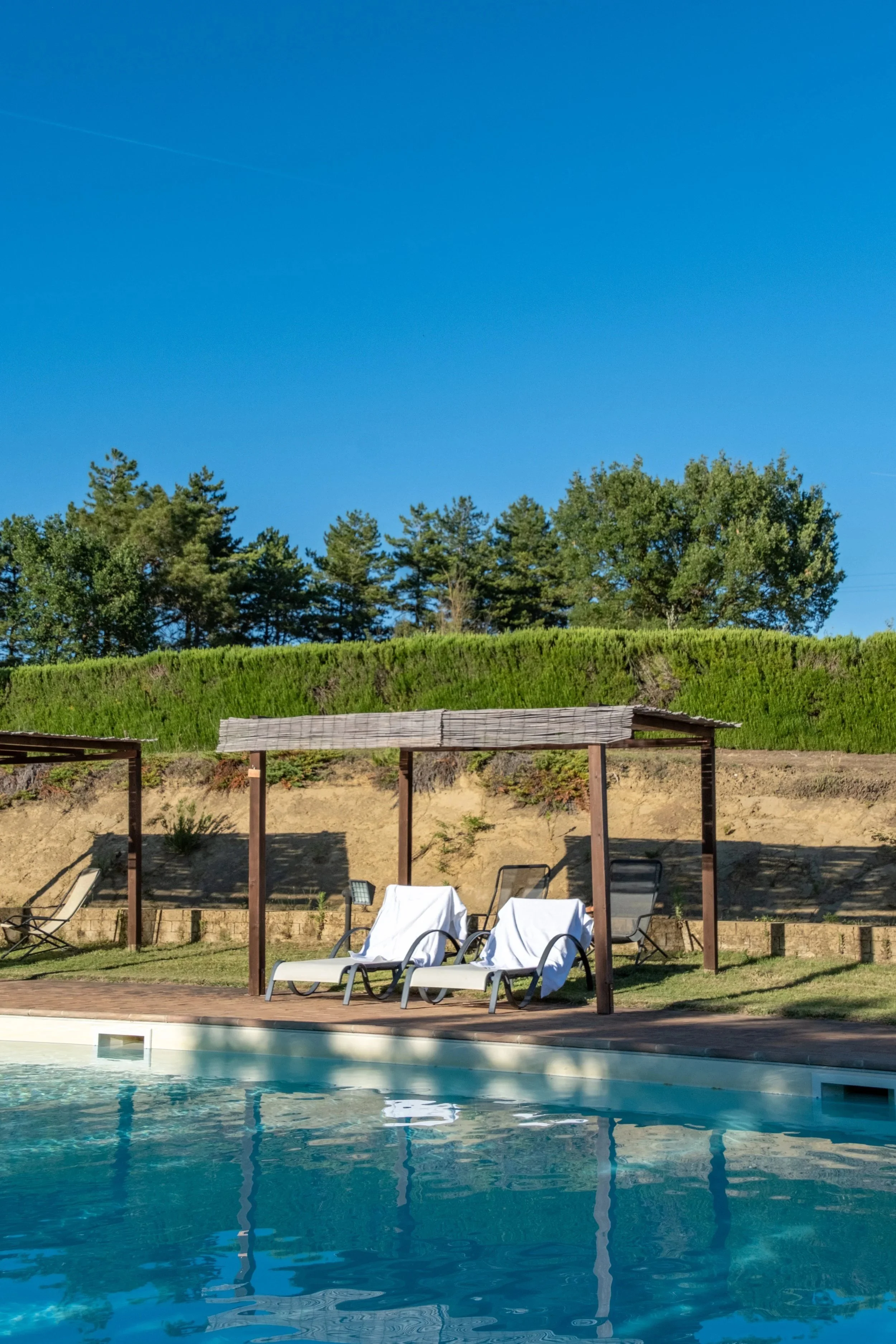 Pool with shaded pergolas and loungers under a blue sky at Agriturismo Selvoli, Val d'Orcia, Tuscany, by Zyan Sachs