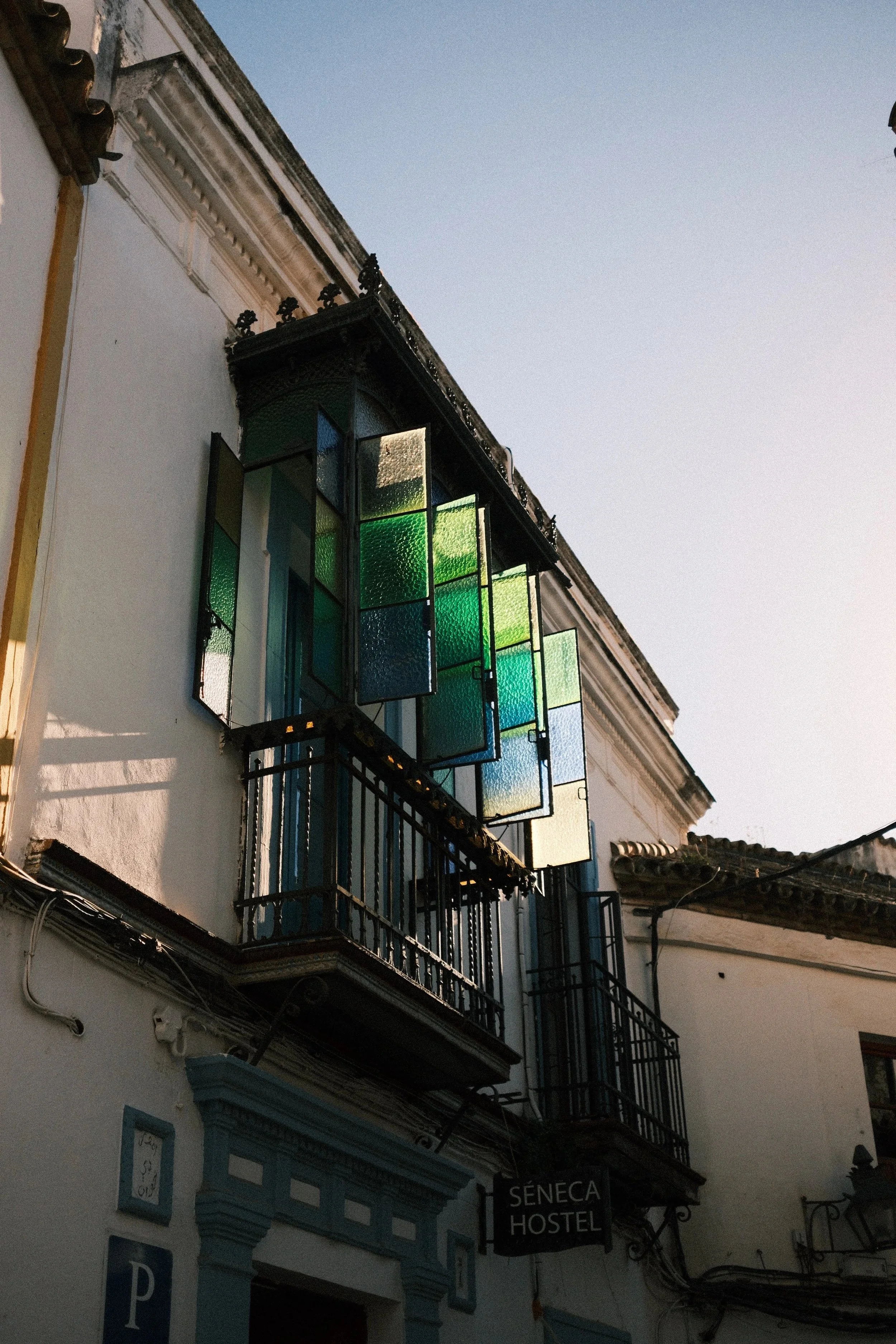 Green stained-glass balcony glowing in the sun above a whitewashed street, Córdoba, Spain, by Zyan Sachs