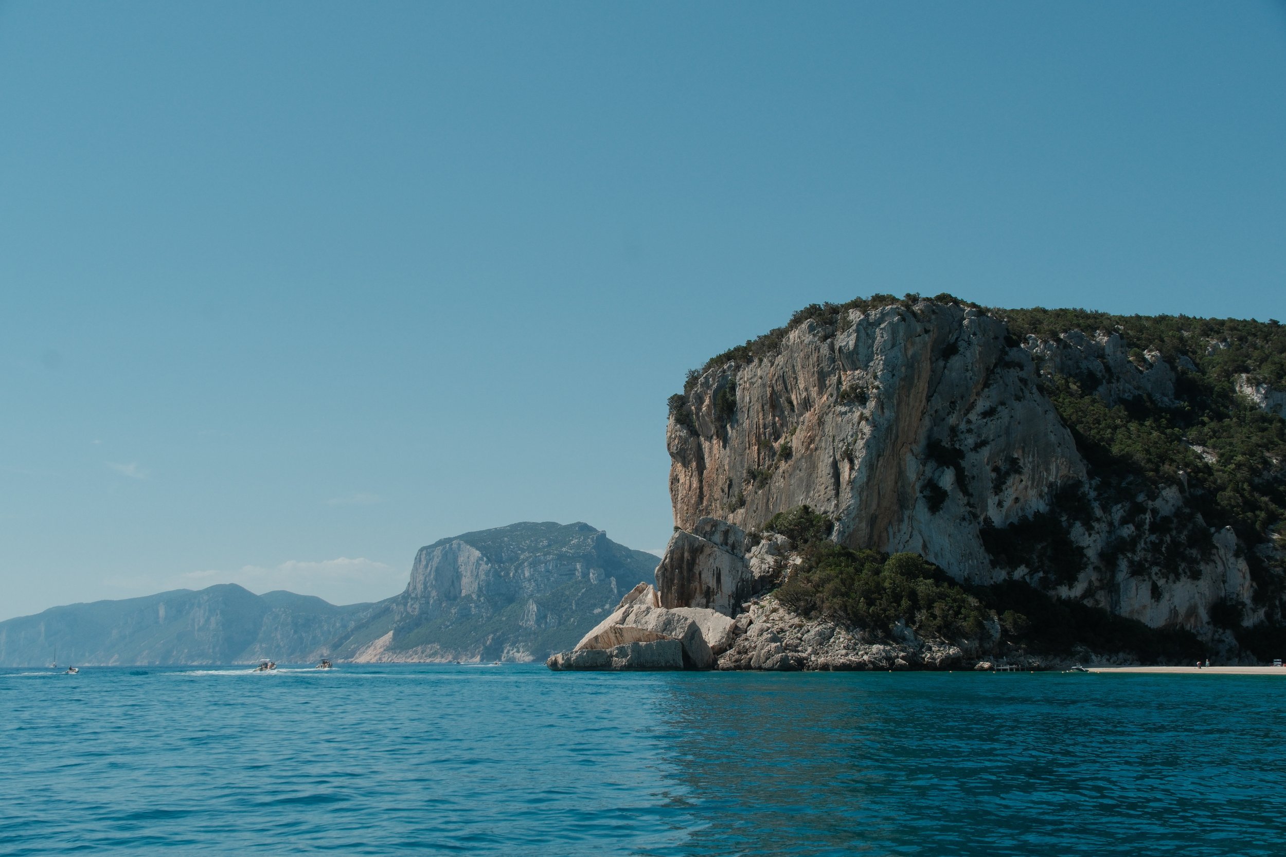 Limestone headland and distant coastal cliffs over calm blue sea, Gulf of Orosei, Sardinia, Italy, by Zyan Sachs