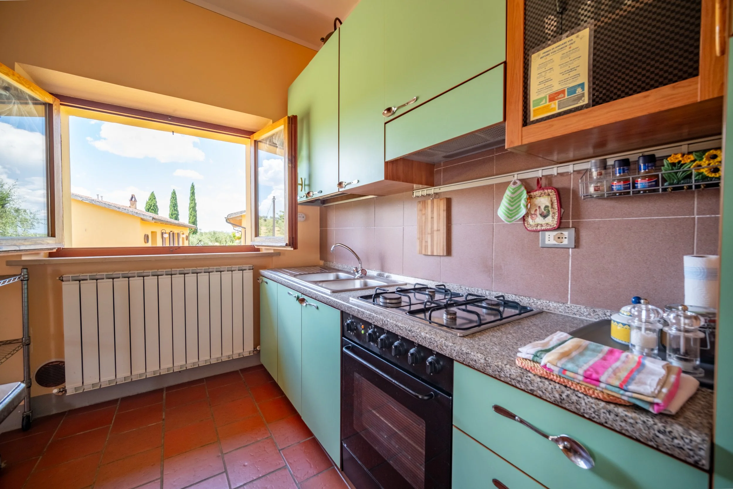 Apartment kitchen with green cabinets and a countryside view at Agriturismo Metina, Montepulciano, Tuscany, by Zyan Sachs