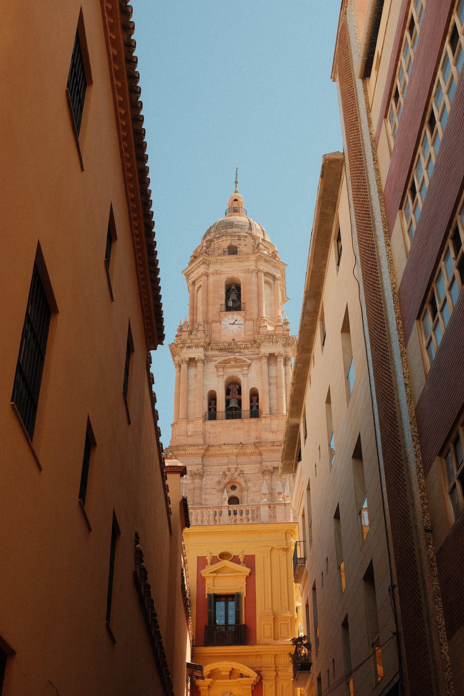 Bell tower of Málaga Cathedral between tall buildings on a narrow street, Málaga, Spain - fine art print by Zyan Sachs