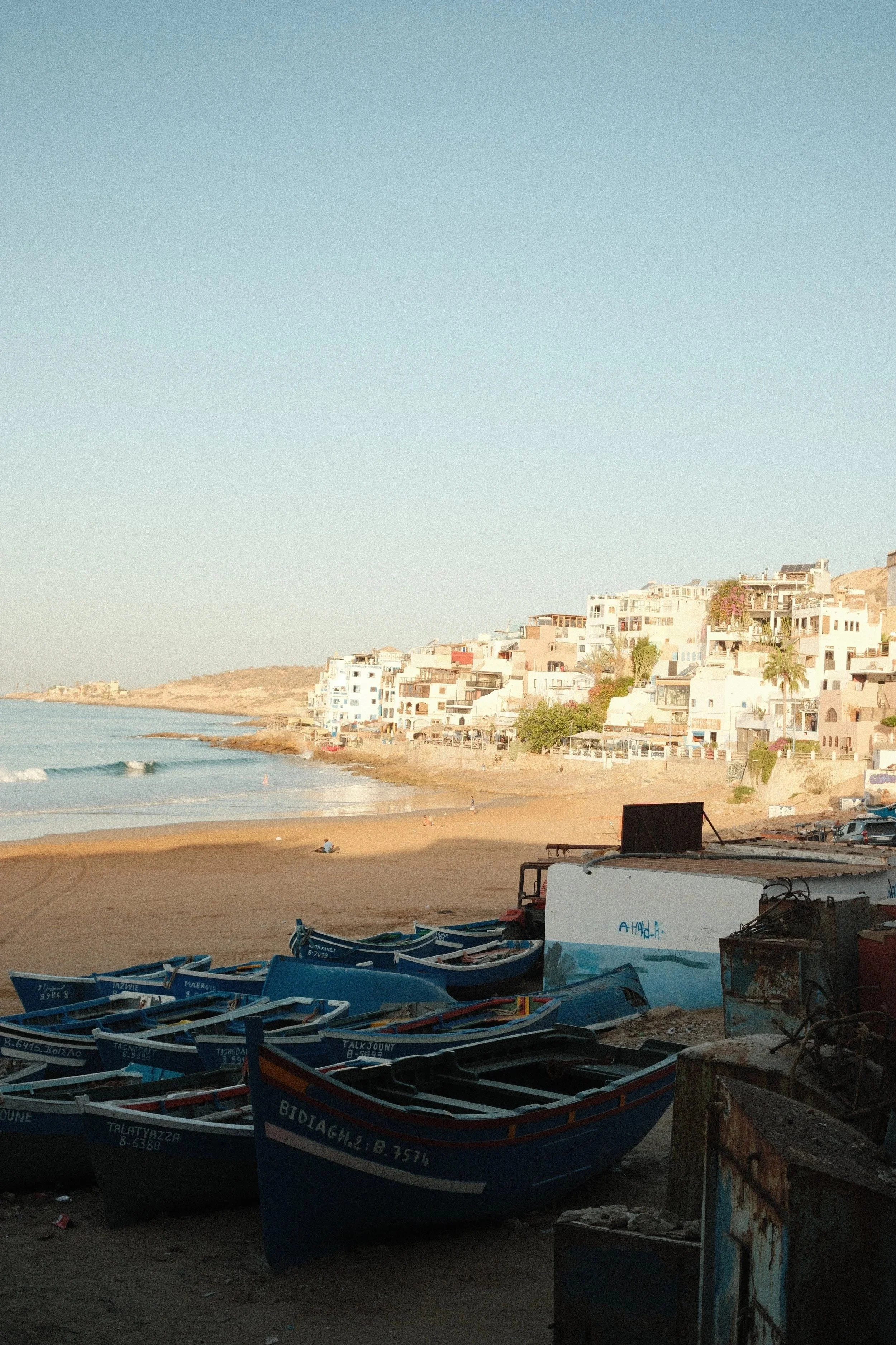 Fishing boats pulled up on the shore below the white town, Taghazout, Morocco - fine art print by Zyan Sachs