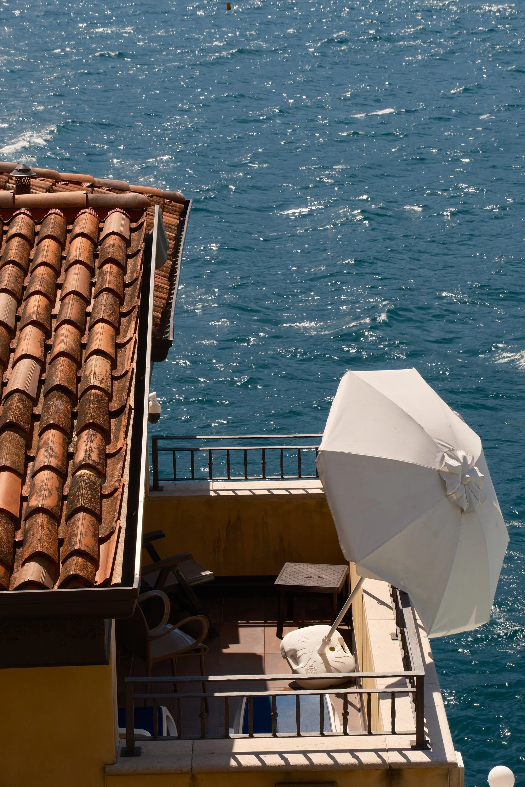 Terracotta roof and balcony with a white umbrella high above sparkling blue water, Lake Garda, Italy, by Zyan Sachs