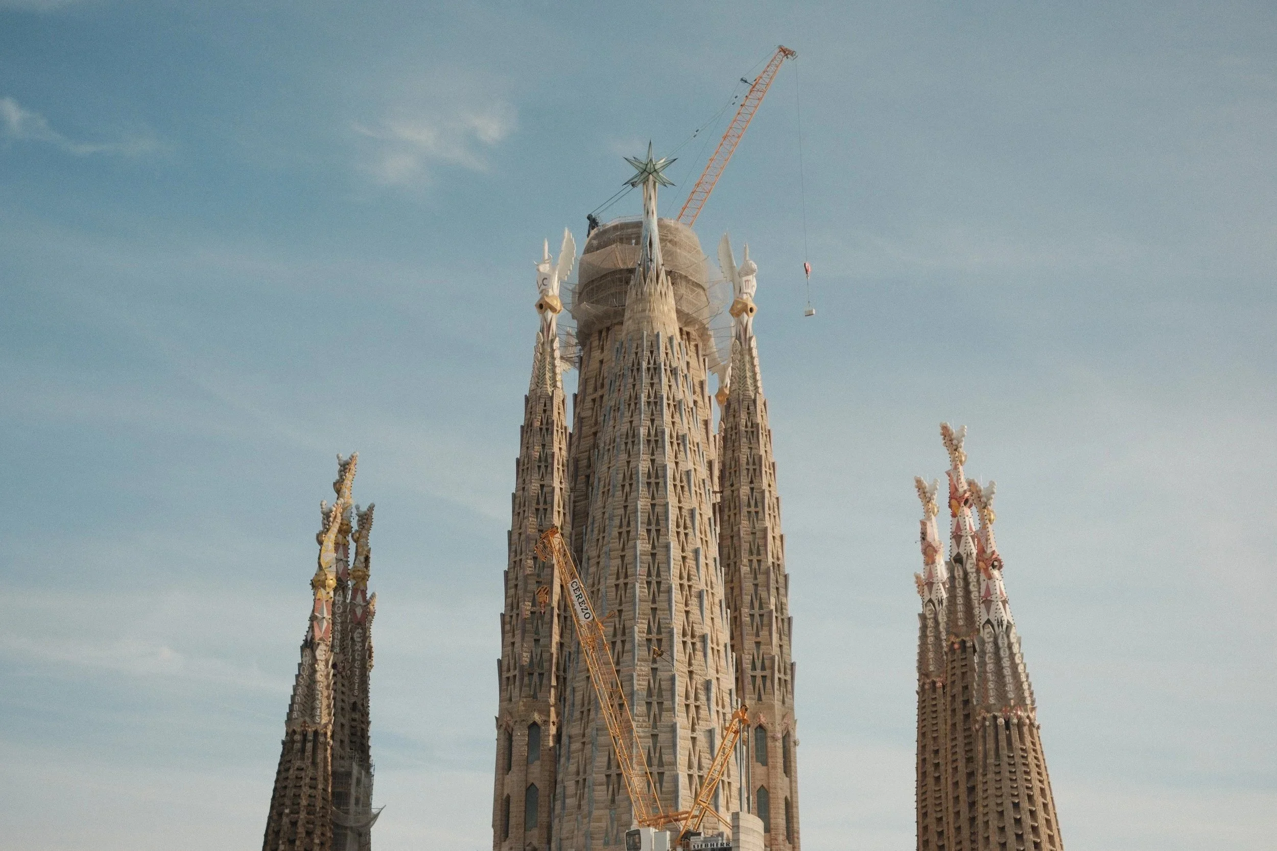 Spires of the Sagrada Família under construction with cranes against a soft sky, Barcelona, Spain, by Zyan Sachs
