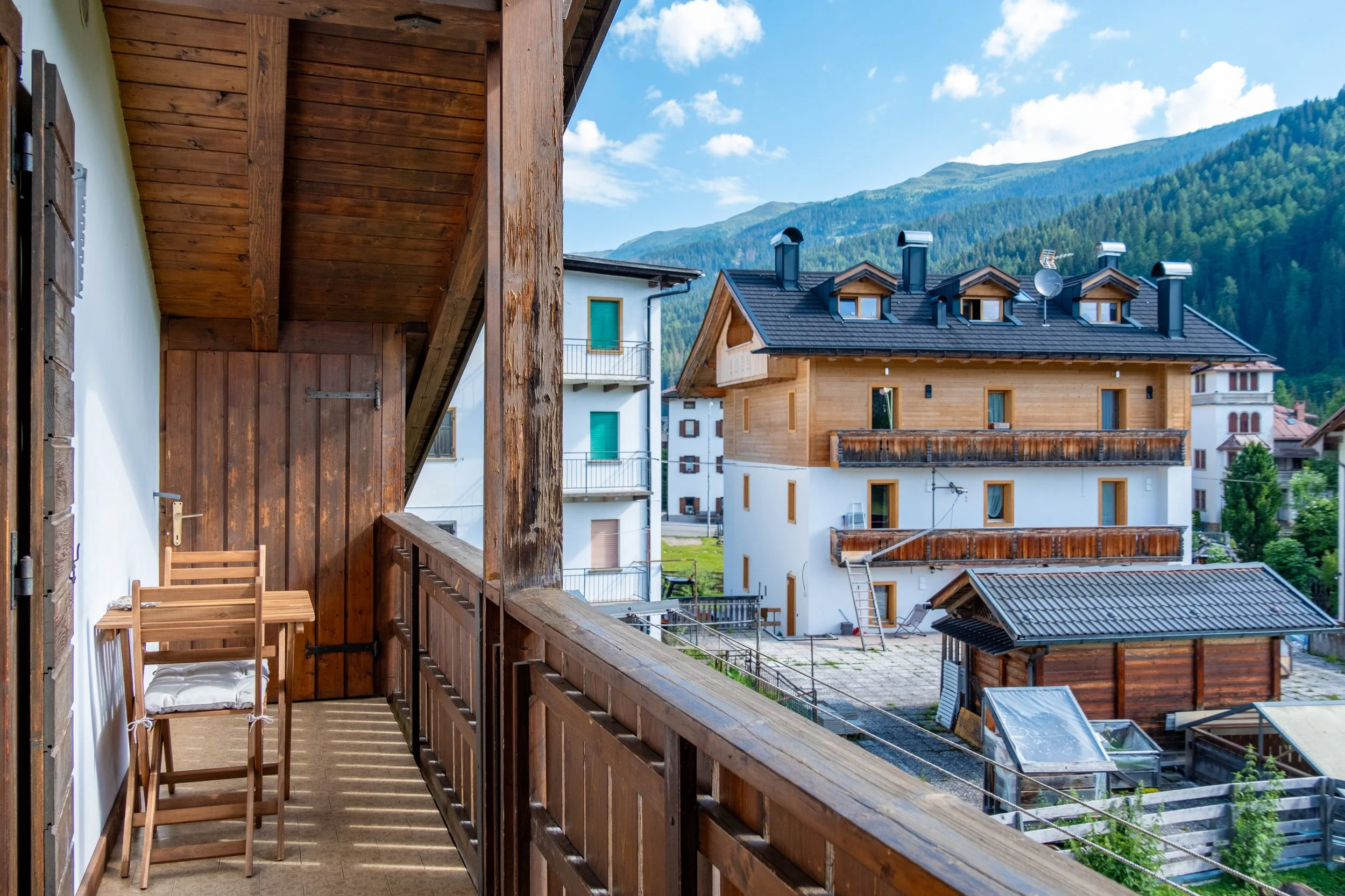 Wooden balcony with a table overlooking village houses and mountains at Al Borgo da Agata, Dolomites, by Zyan Sachs