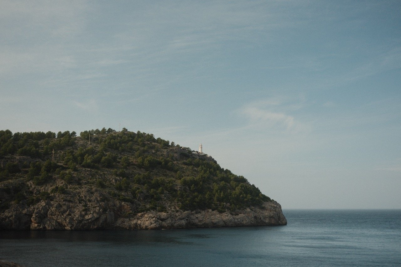 Pine-covered headland on a calm, misty sea, Mallorca, Spain, by Zyan Sachs