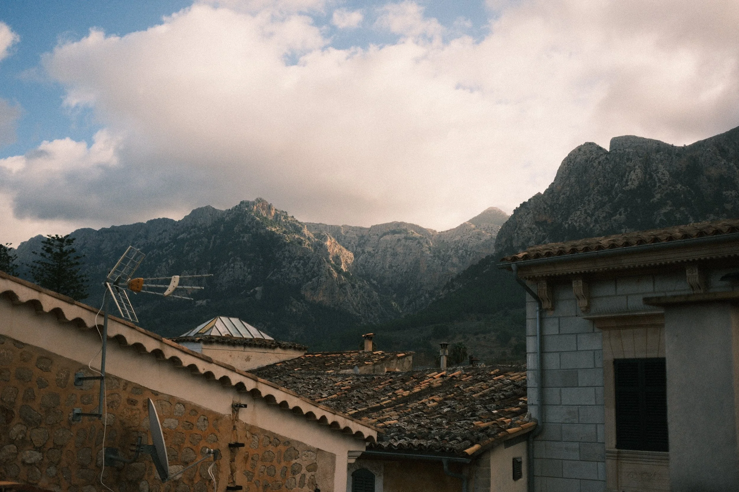 Stone village rooftops below the Tramuntana mountains under billowing clouds, Mallorca, Spain, by Zyan Sachs