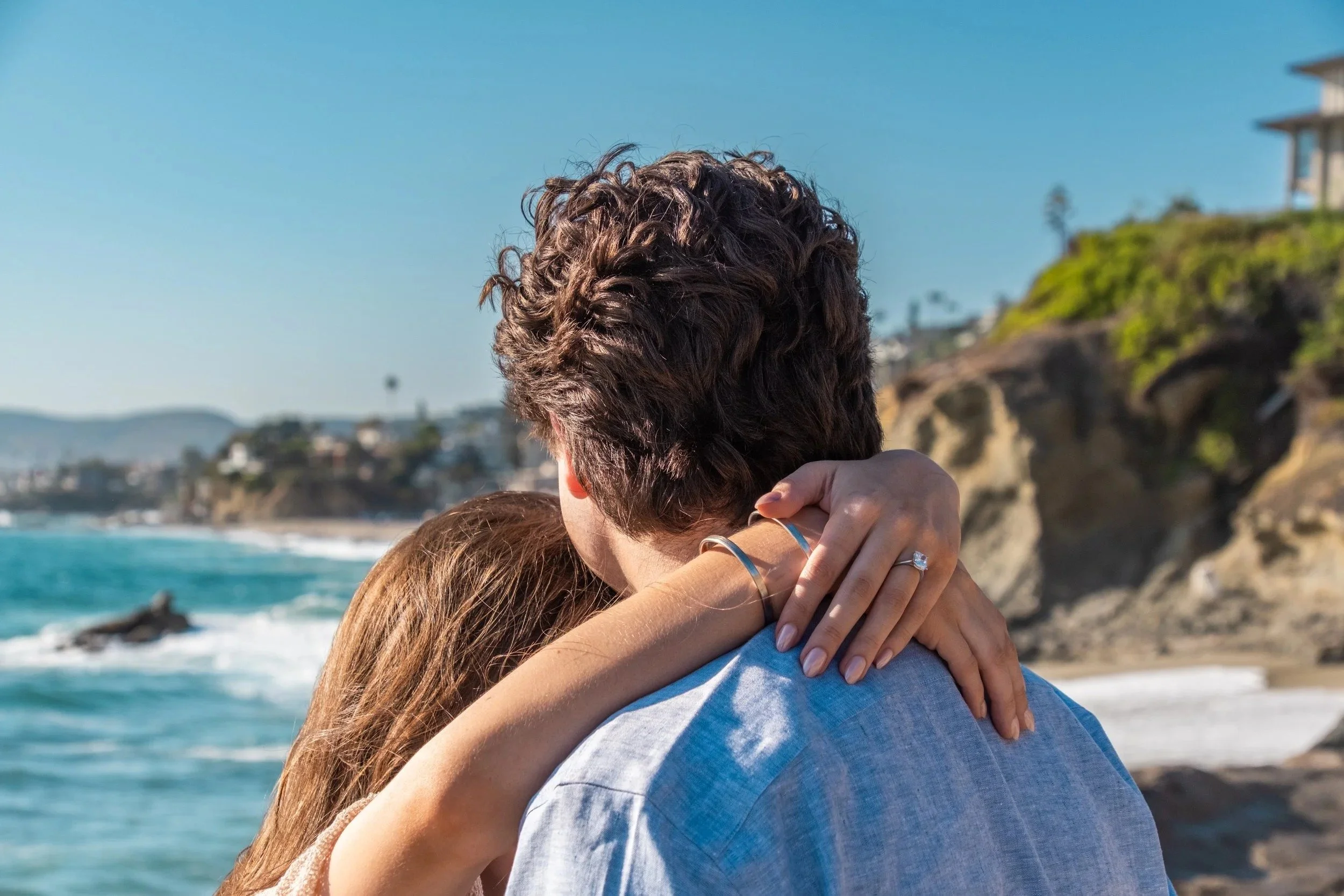 Newly engaged couple embracing by the ocean, ring on her hand, Southern California - proposal photography by Zyan Sachs