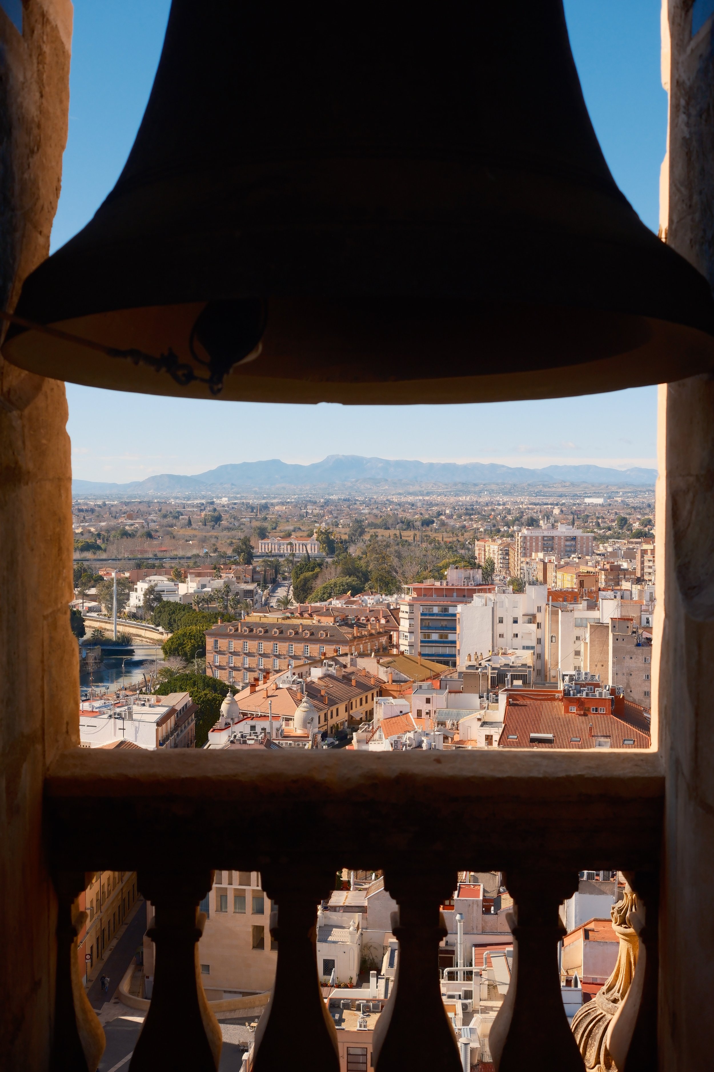 View over Murcia and distant mountains framed by a bell in the cathedral tower, Murcia, Spain, by Zyan Sachs
