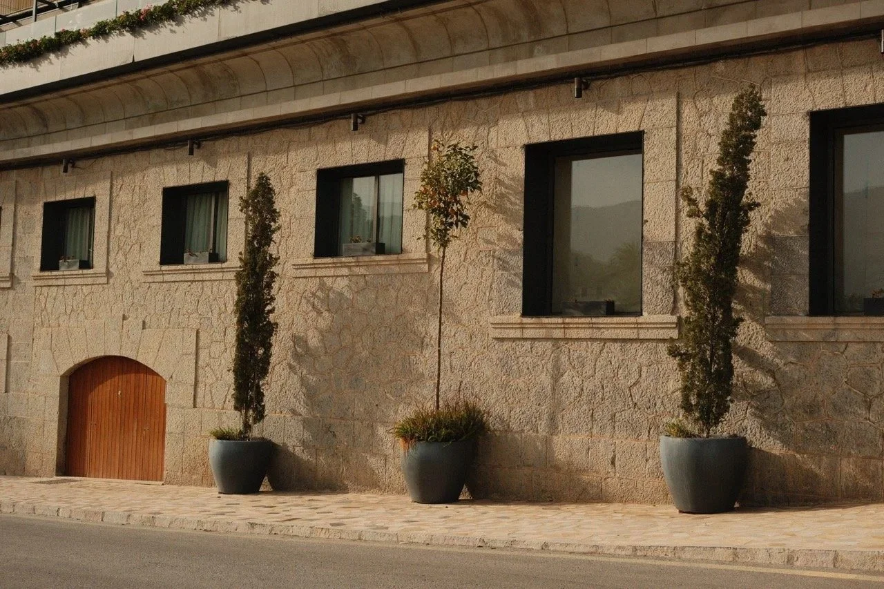 Sandstone building with green shutters and potted cypresses on a quiet street, Mallorca, Spain - fine art print by Zyan Sachs