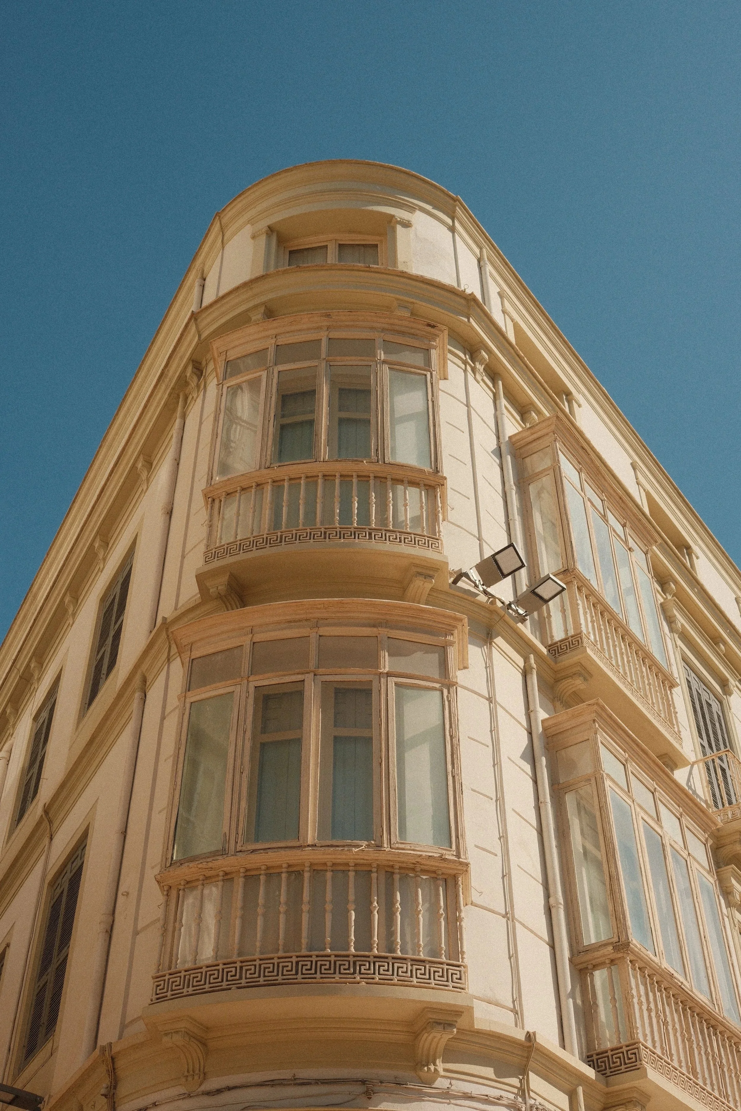 Cream corner building with rounded glass balconies against a blue sky, Málaga, Spain, by Zyan Sachs