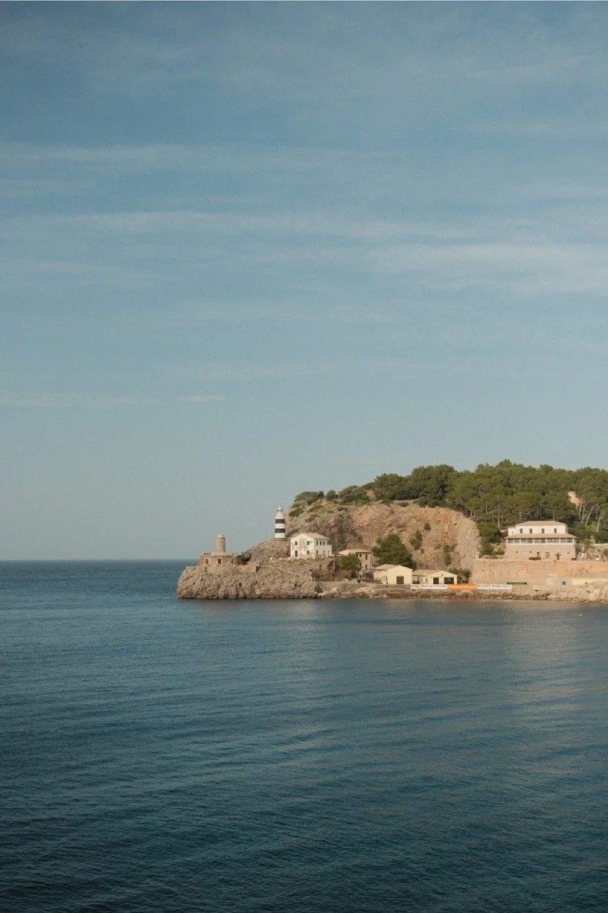 Coastal village and lighthouse point across a still blue bay, Mallorca, Spain, by Zyan Sachs