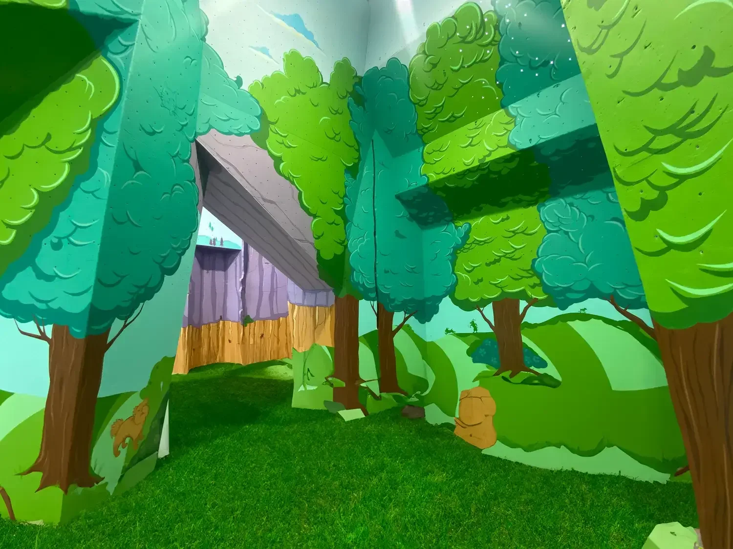 Colorful indoor dog park at Pawsome Park and Lodge with artificial turf, painted forest walls, and open play space for dogs