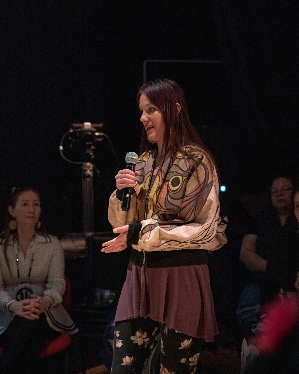 Person standing front of audience with a microphone in hand.