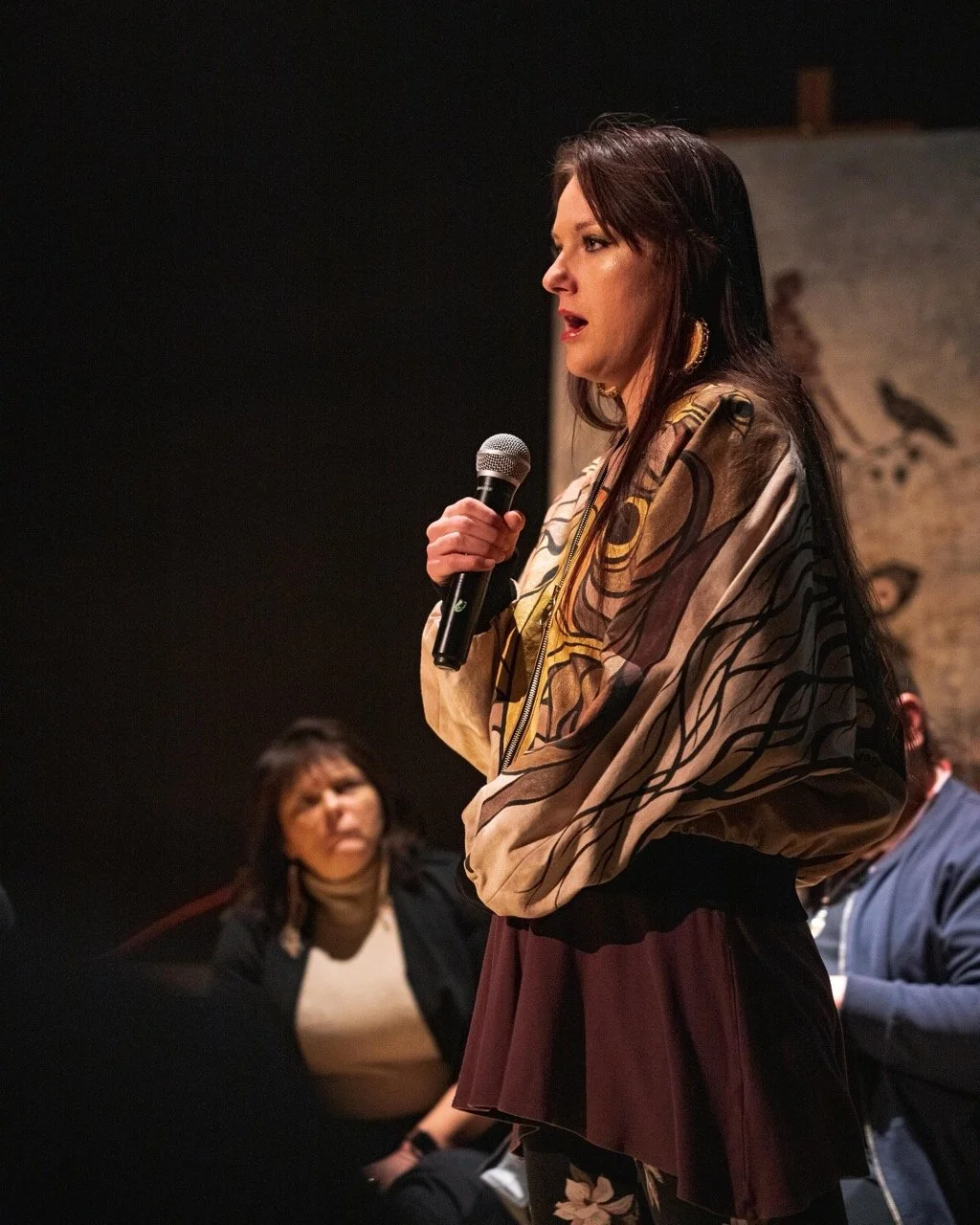 Person standing front of audience with a microphone in hand.
